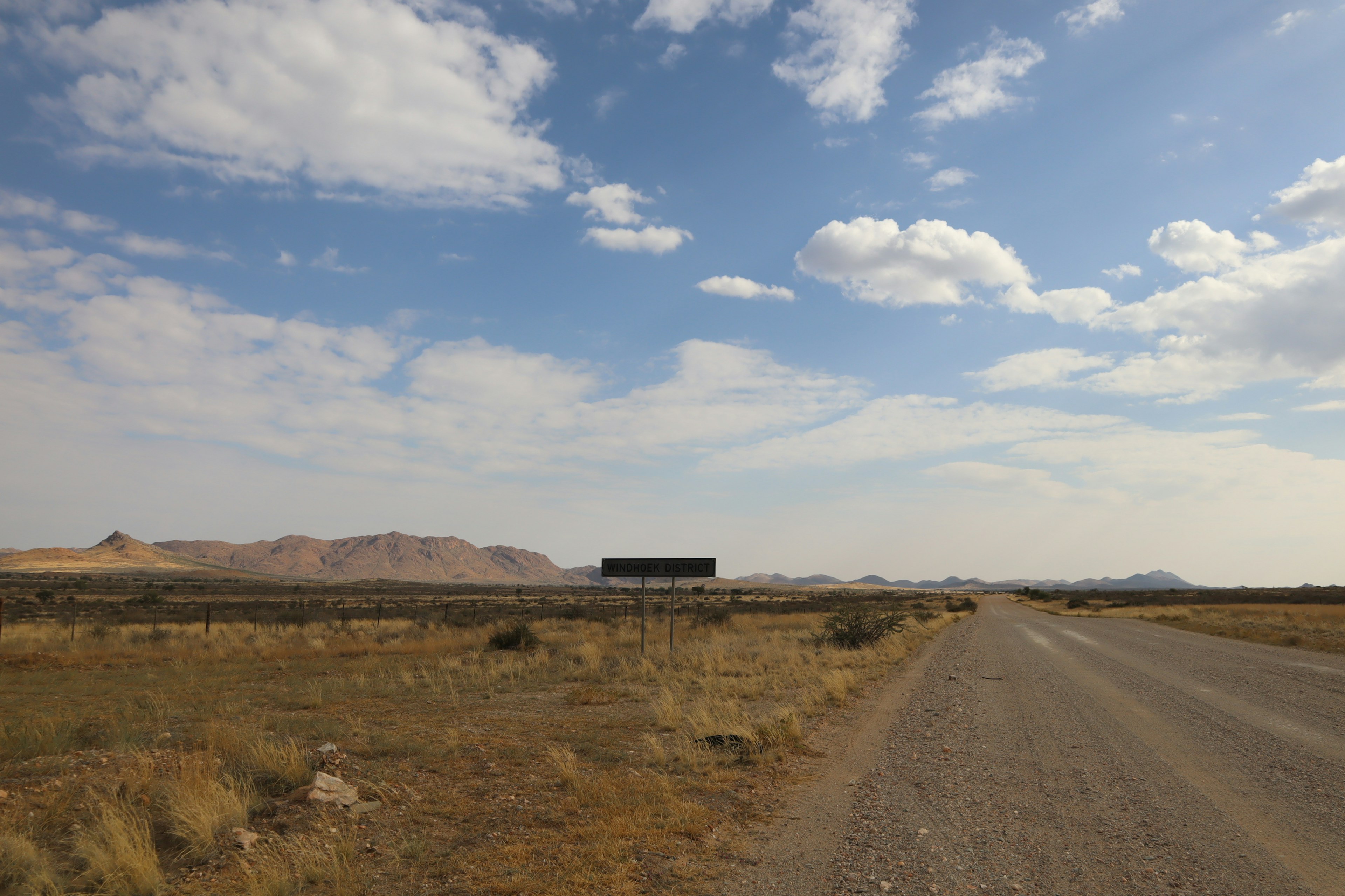 Scenic view of a gravel road under a blue sky with scattered clouds