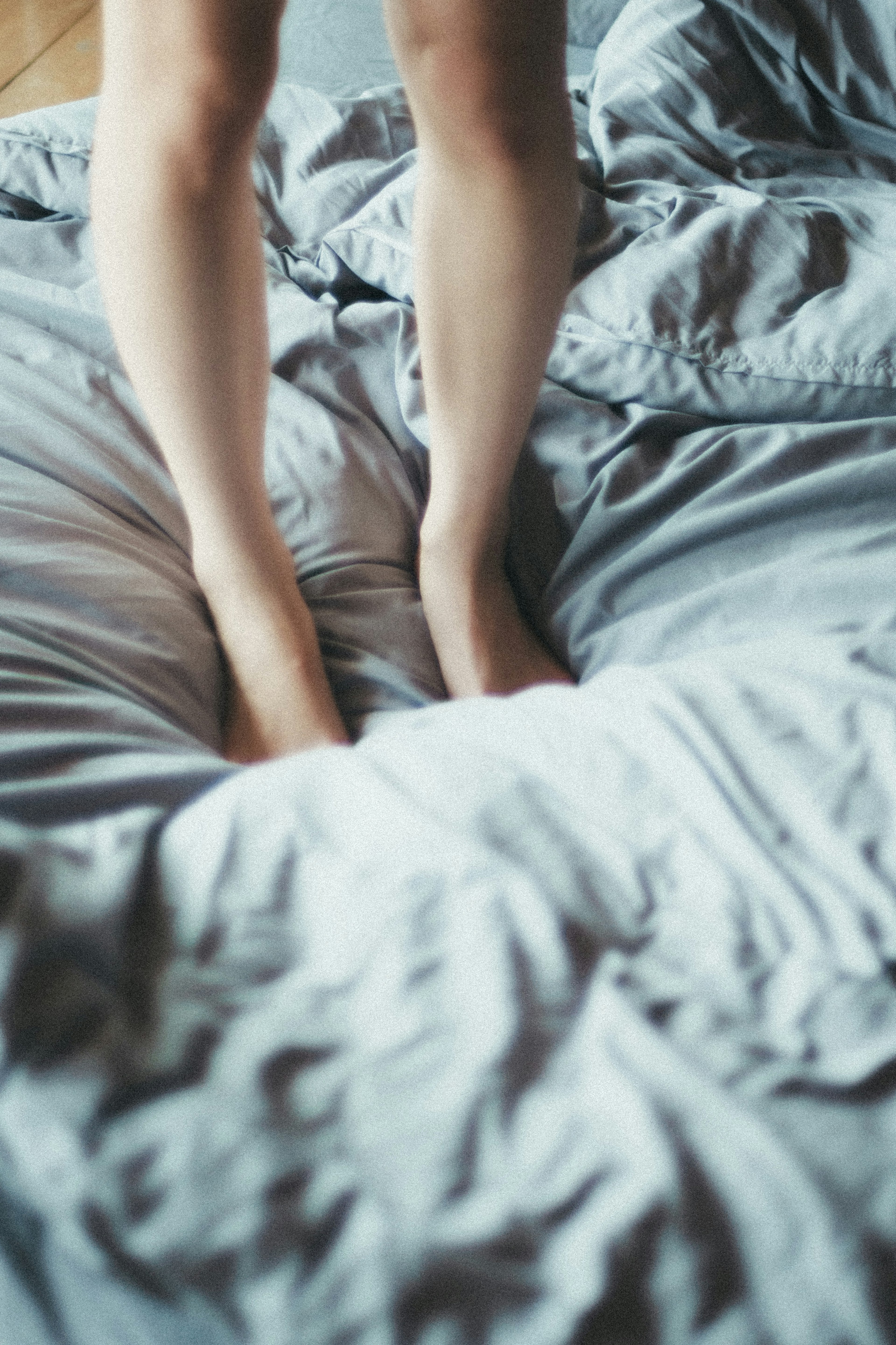 Bare feet of a person standing on wrinkled bedding