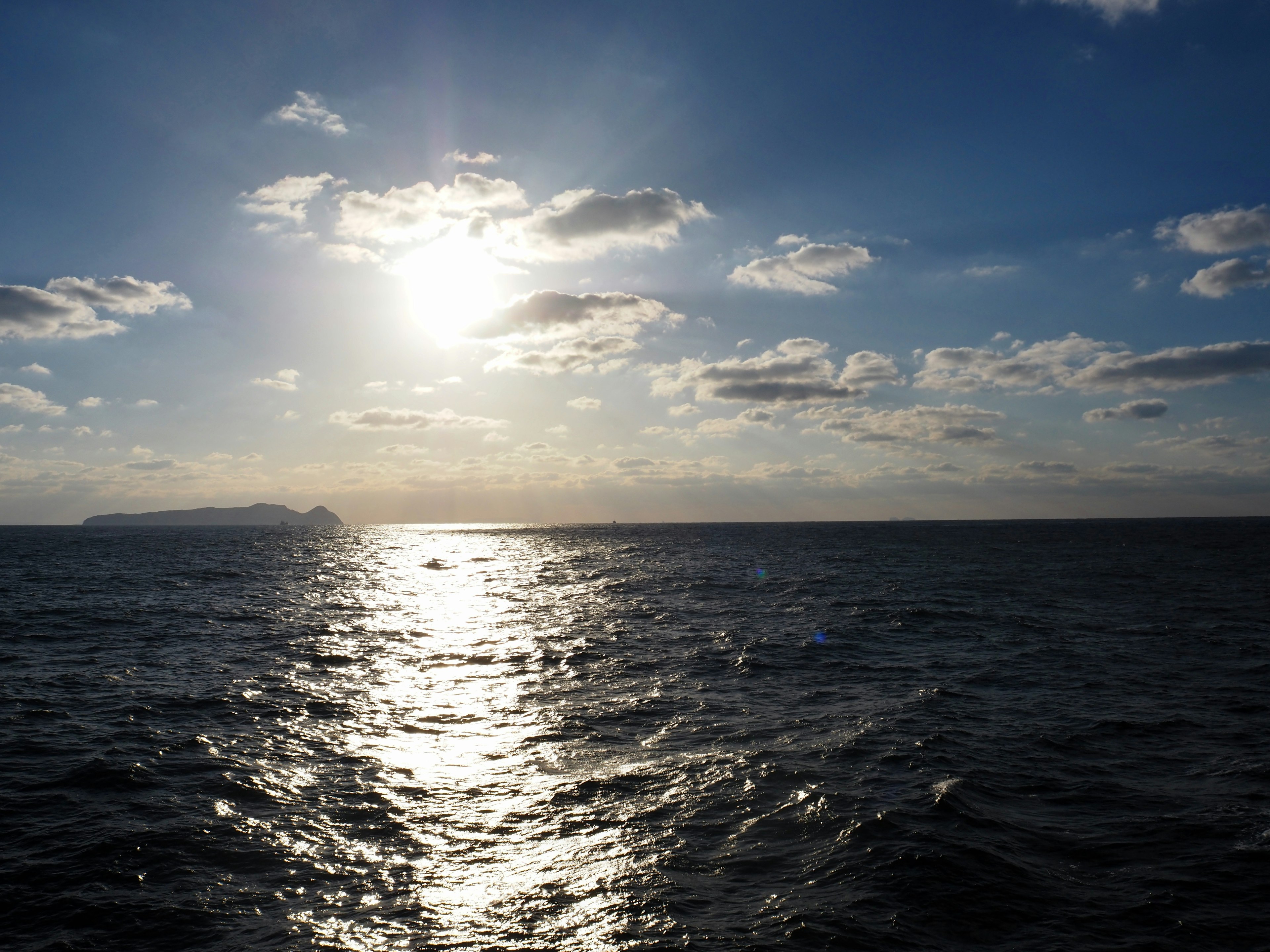 Bright sun shining over the ocean with clouds in a blue sky