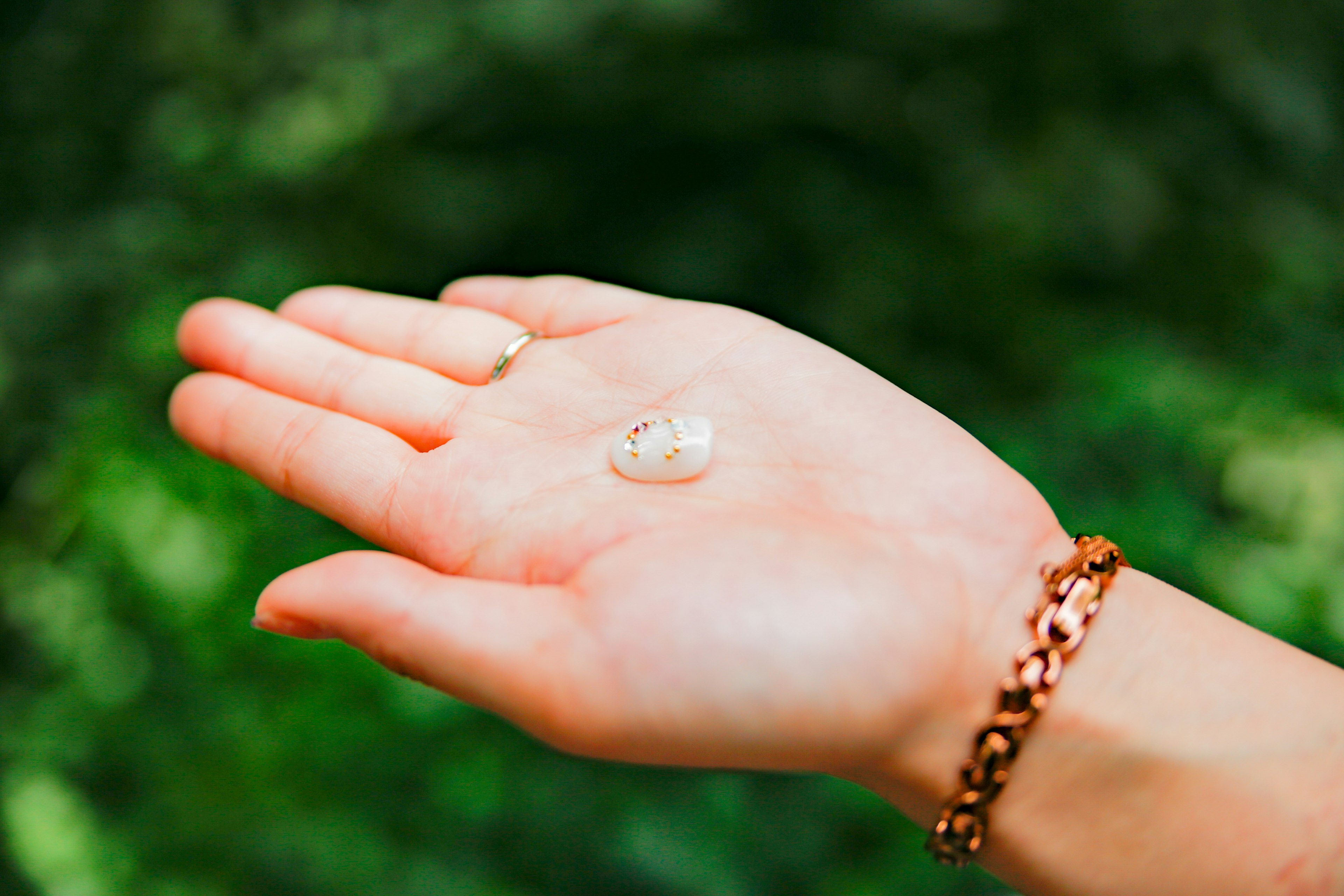 A hand holding a transparent stone-like object with a bracelet on the wrist