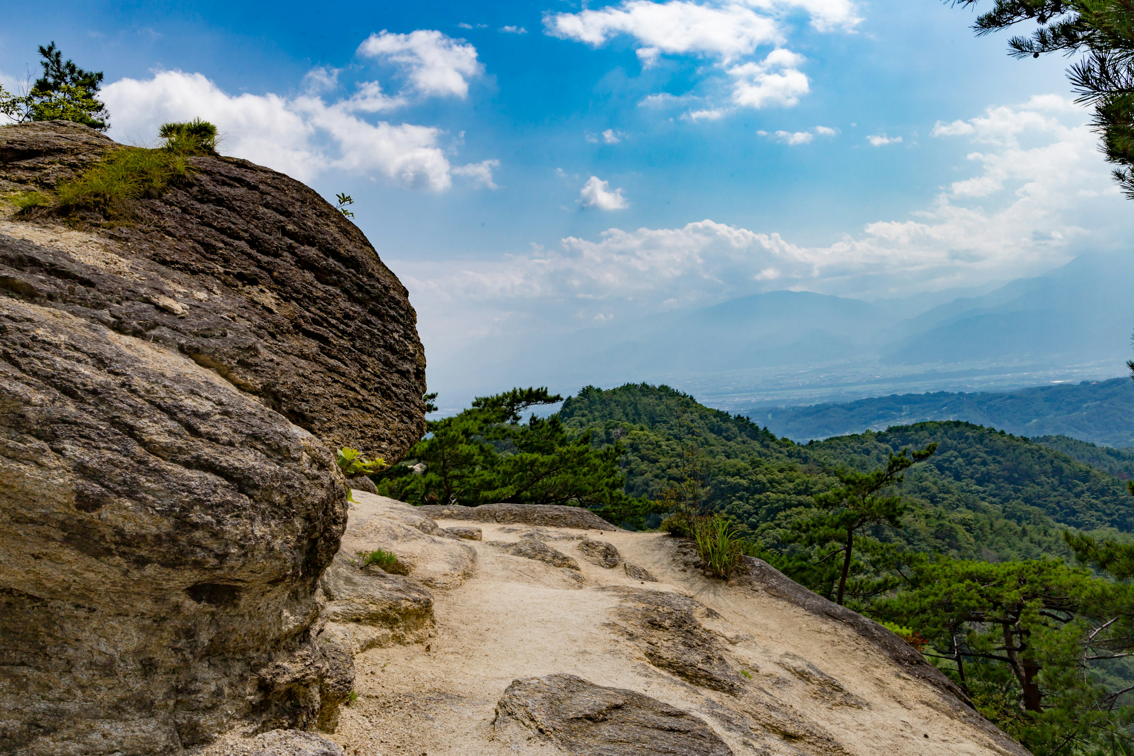 蓝天下岩石山脉的风景，绿色树木和远处的山丘