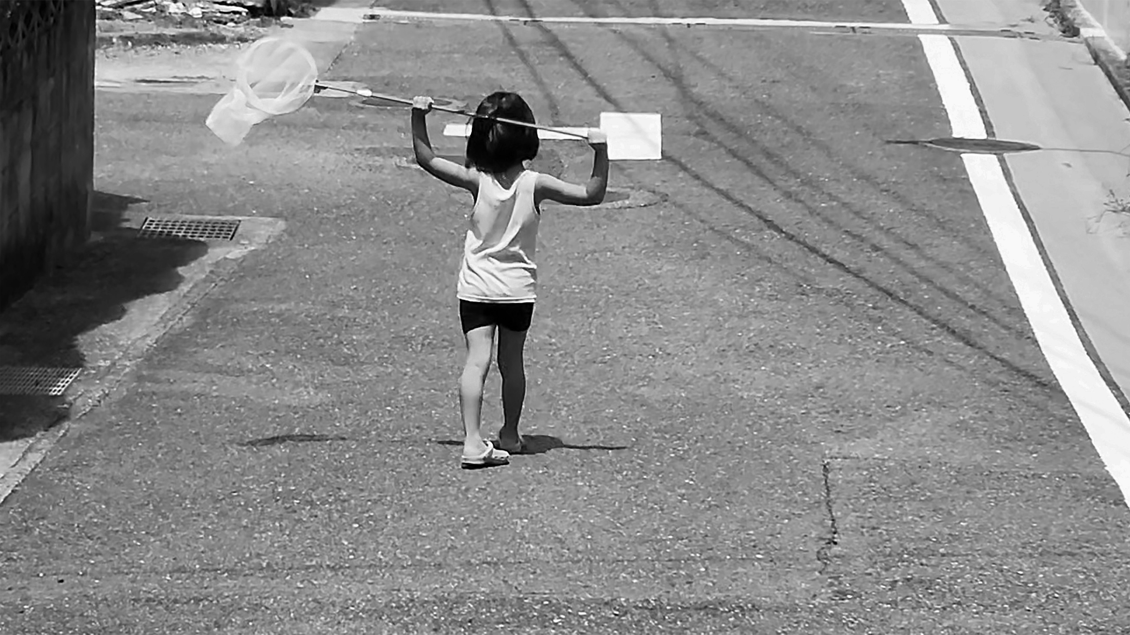 A child walking with a net on a road in black and white