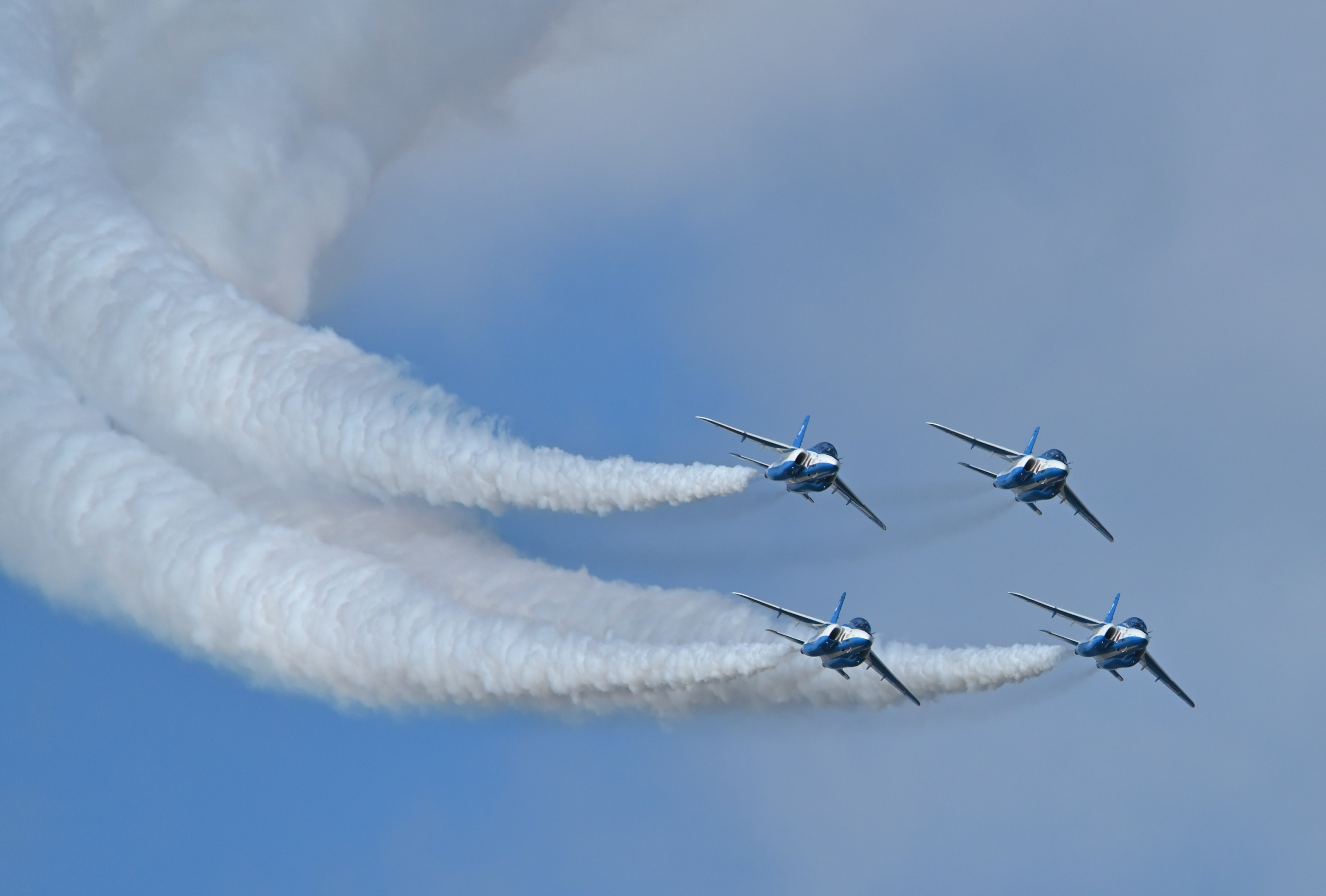 Blaue Kampfjets fliegen in Formation und hinterlassen weiße Rauchspuren am Himmel