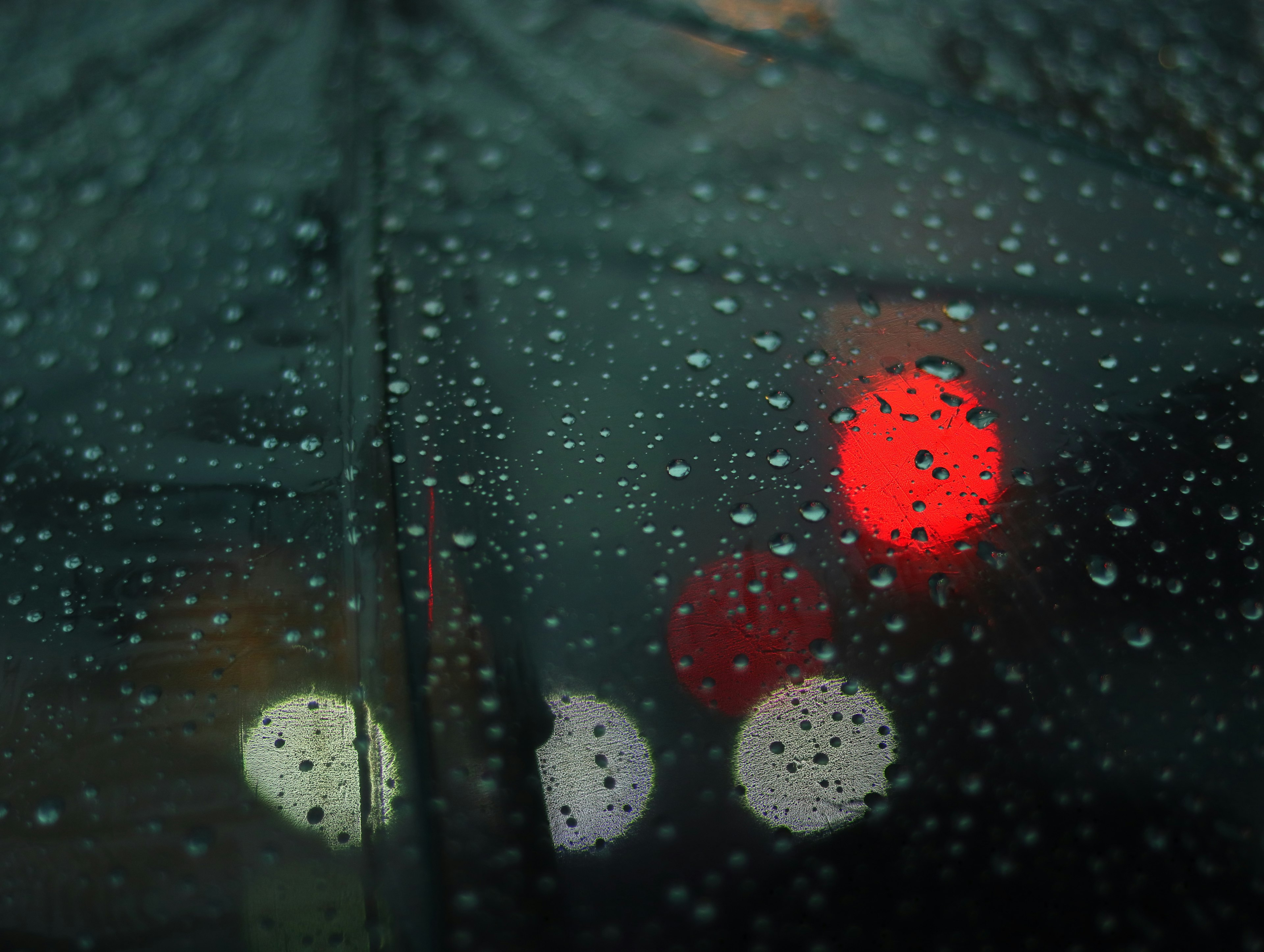 Vista a través de un paraguas cubierto de lluvia mostrando luces rojas y blancas