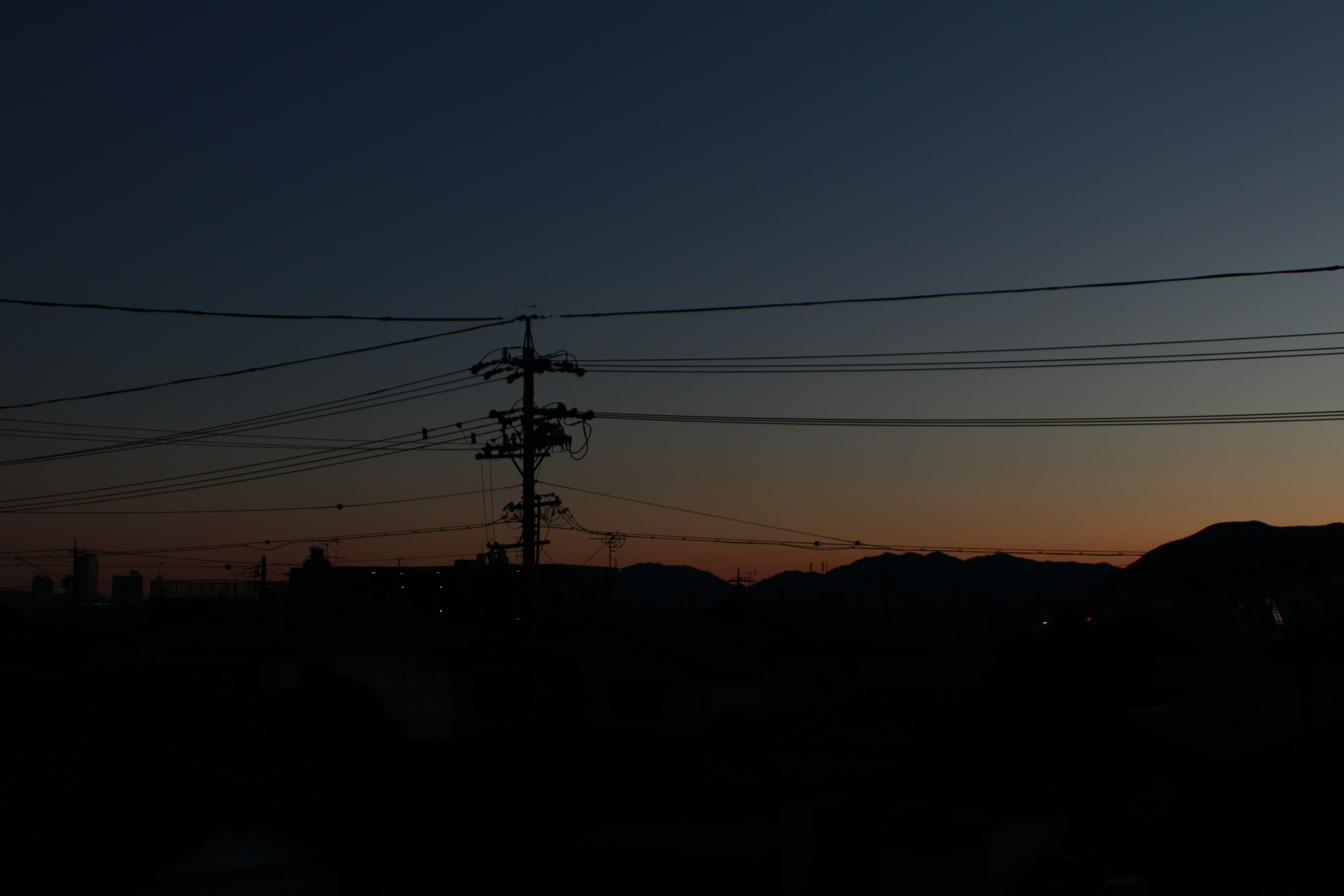 Paysage du crépuscule avec des lignes et des poteaux électriques silhouettés contre des montagnes