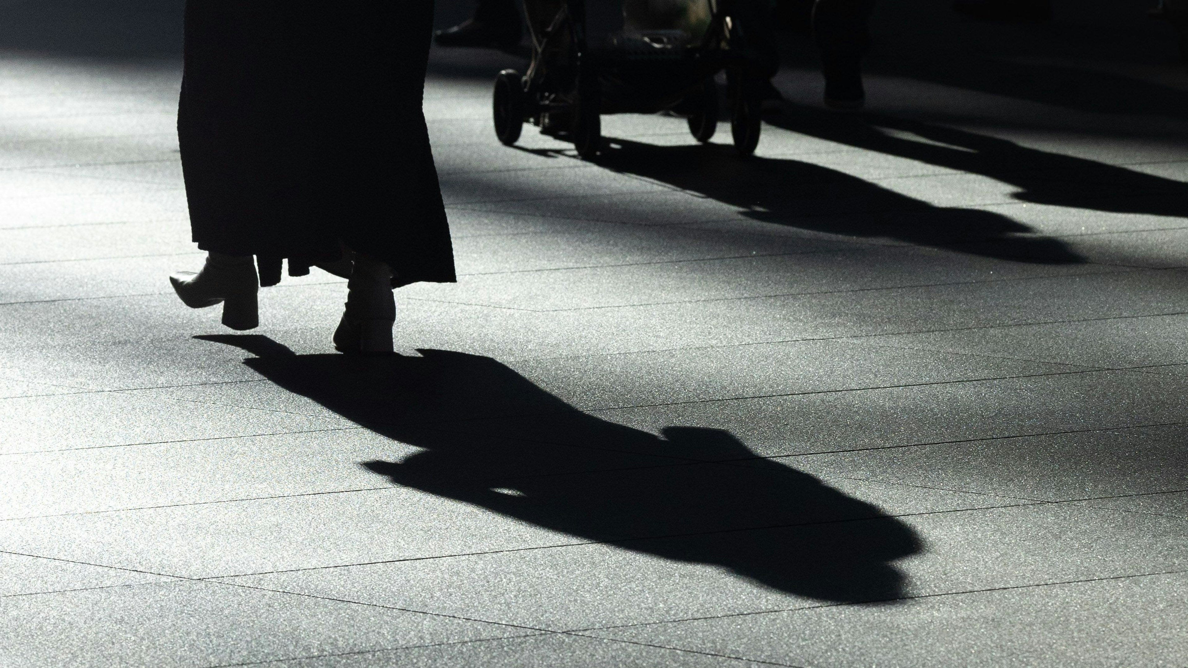 Una persona vestida de negro caminando con una sombra proyectada en el pavimento