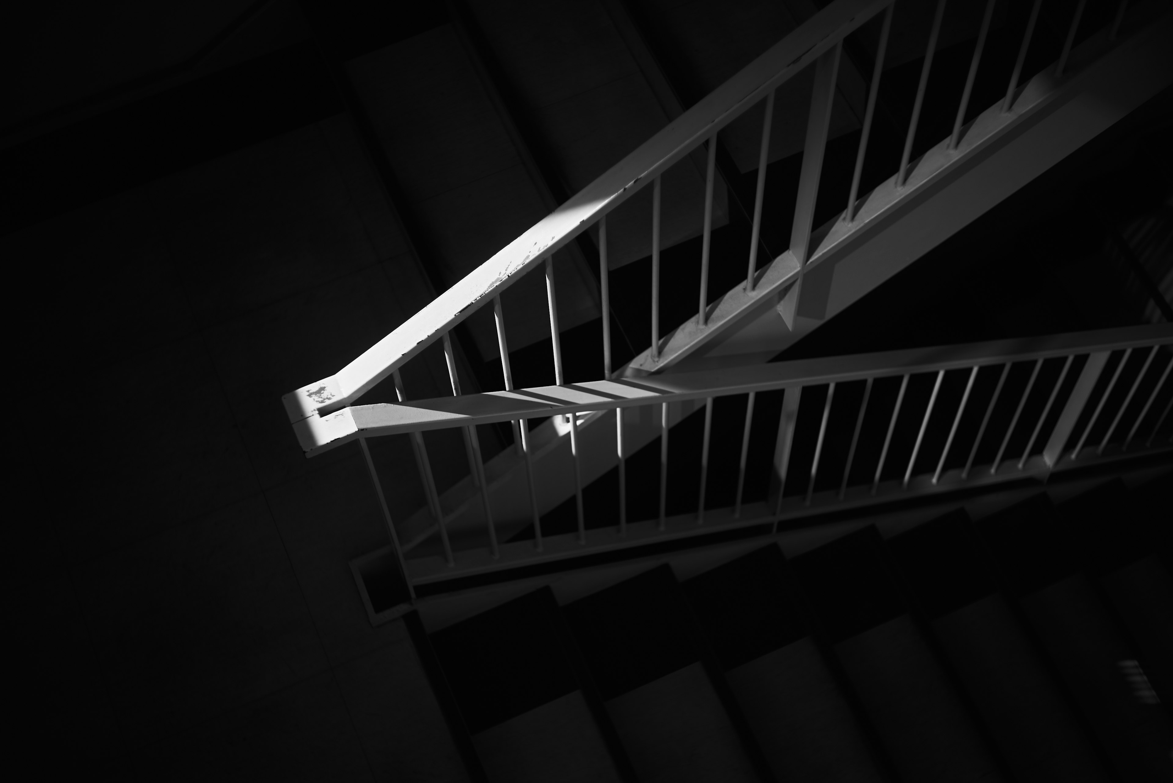 Imagen en blanco y negro de escaleras con barandilla blanca y sombras marcadas