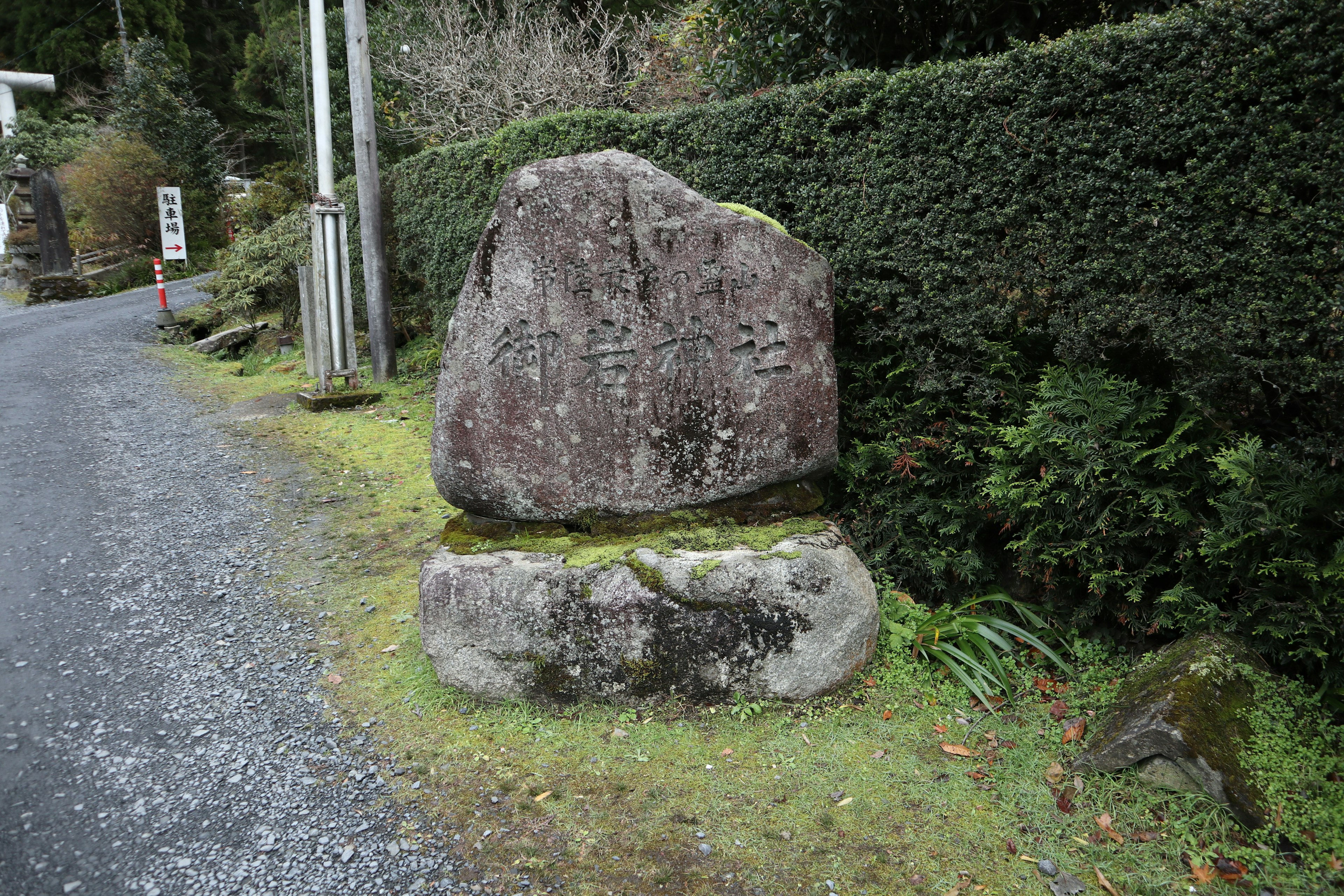 A stone monument beside a gravel road surrounded by greenery and moss