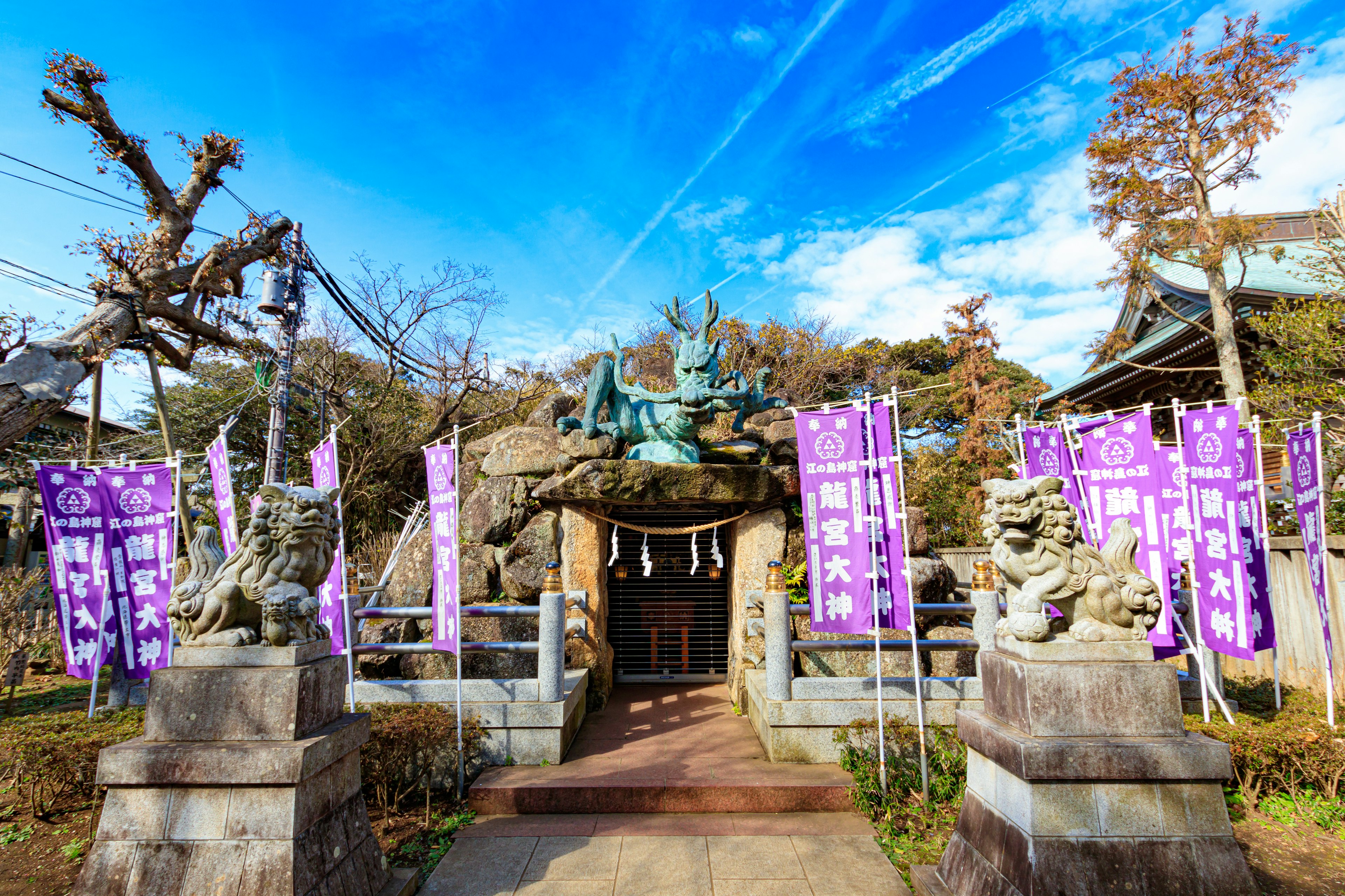 神社の入り口にある狛犬と紫の旗 青空と木々が背景の風景