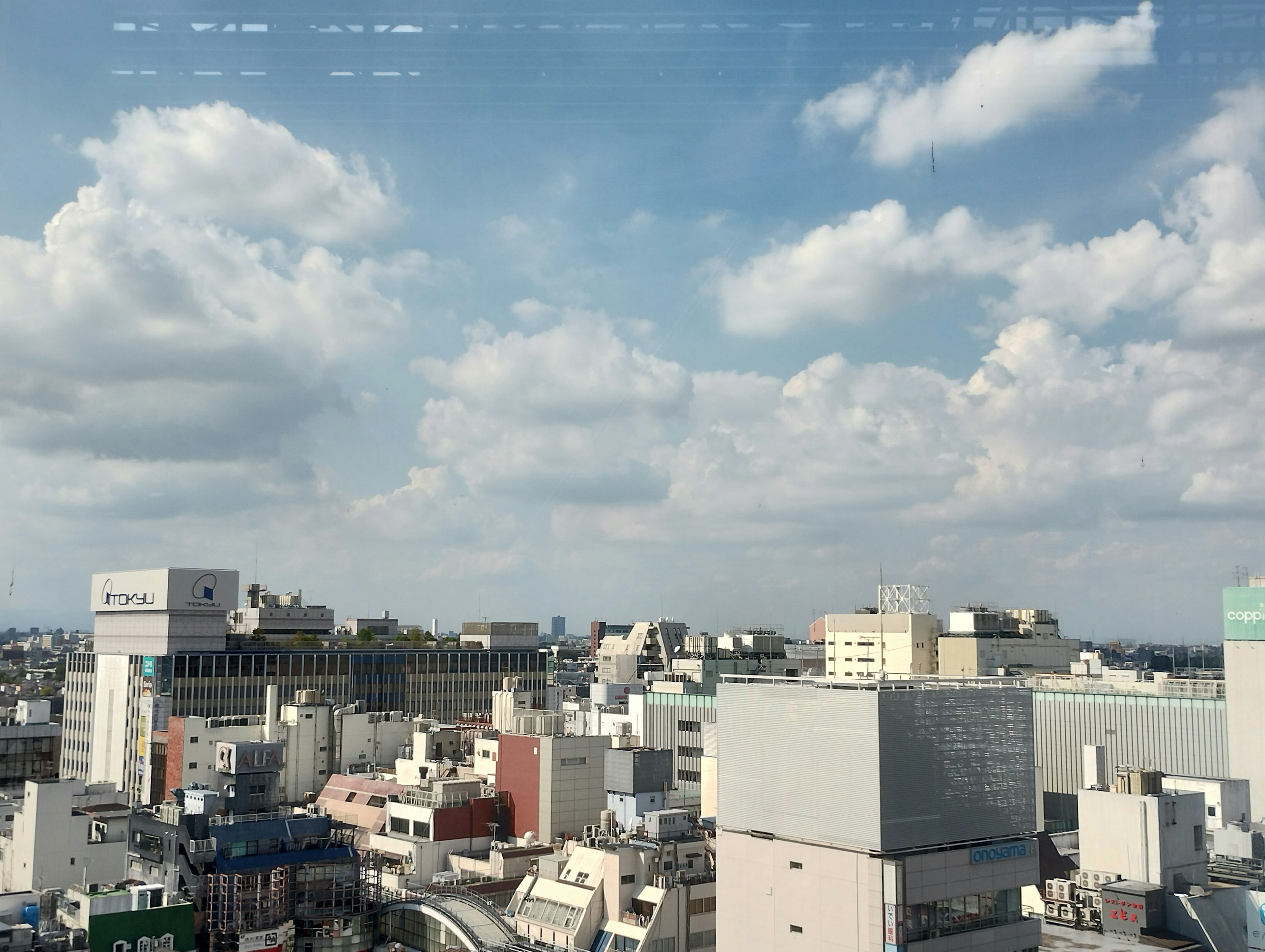 高層ビルからの都市の景色、青空と白い雲が広がる