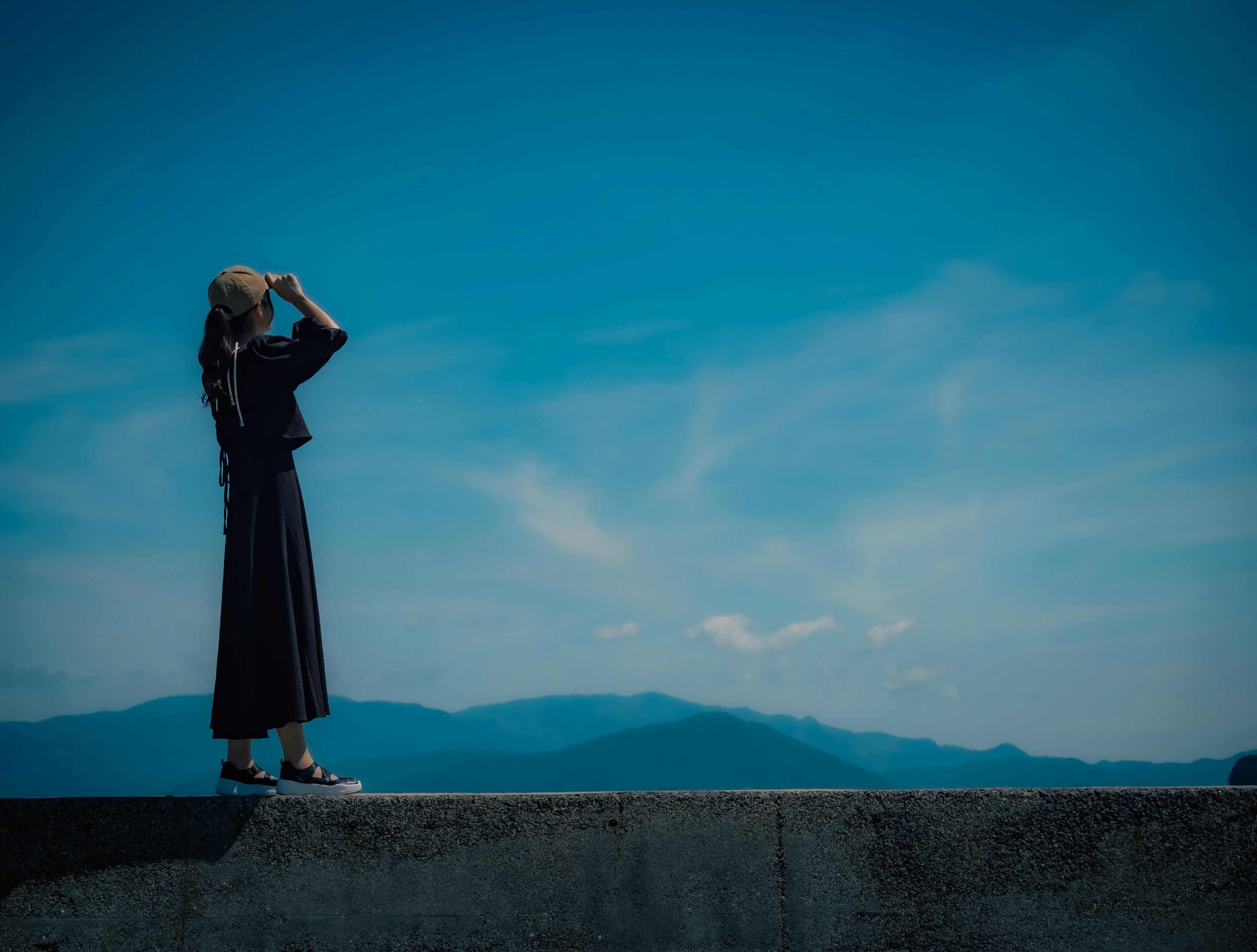 Silhouette einer Frau, die unter einem blauen Himmel in die Ferne schaut