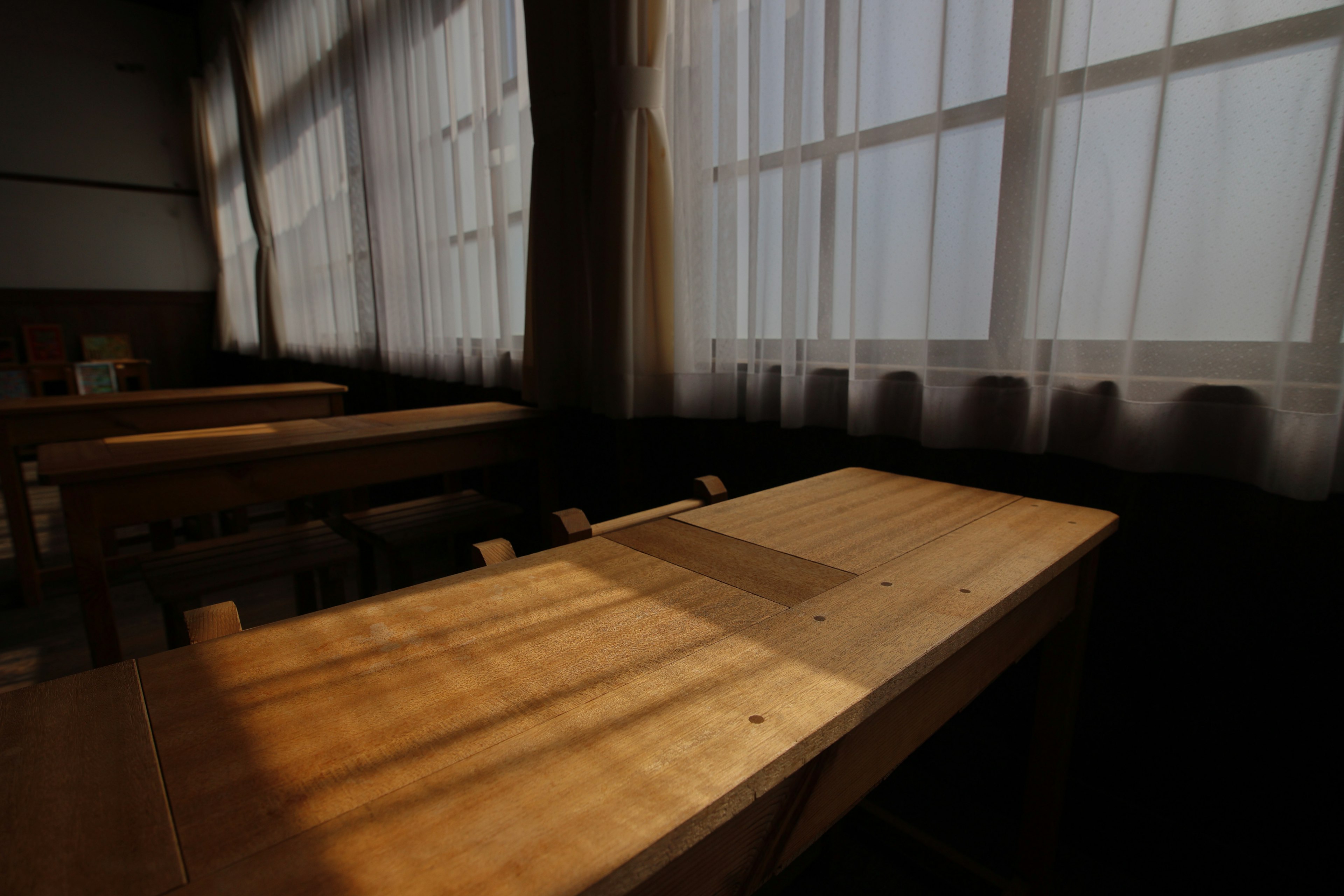 Wooden table in a classroom with sunlight streaming through sheer curtains