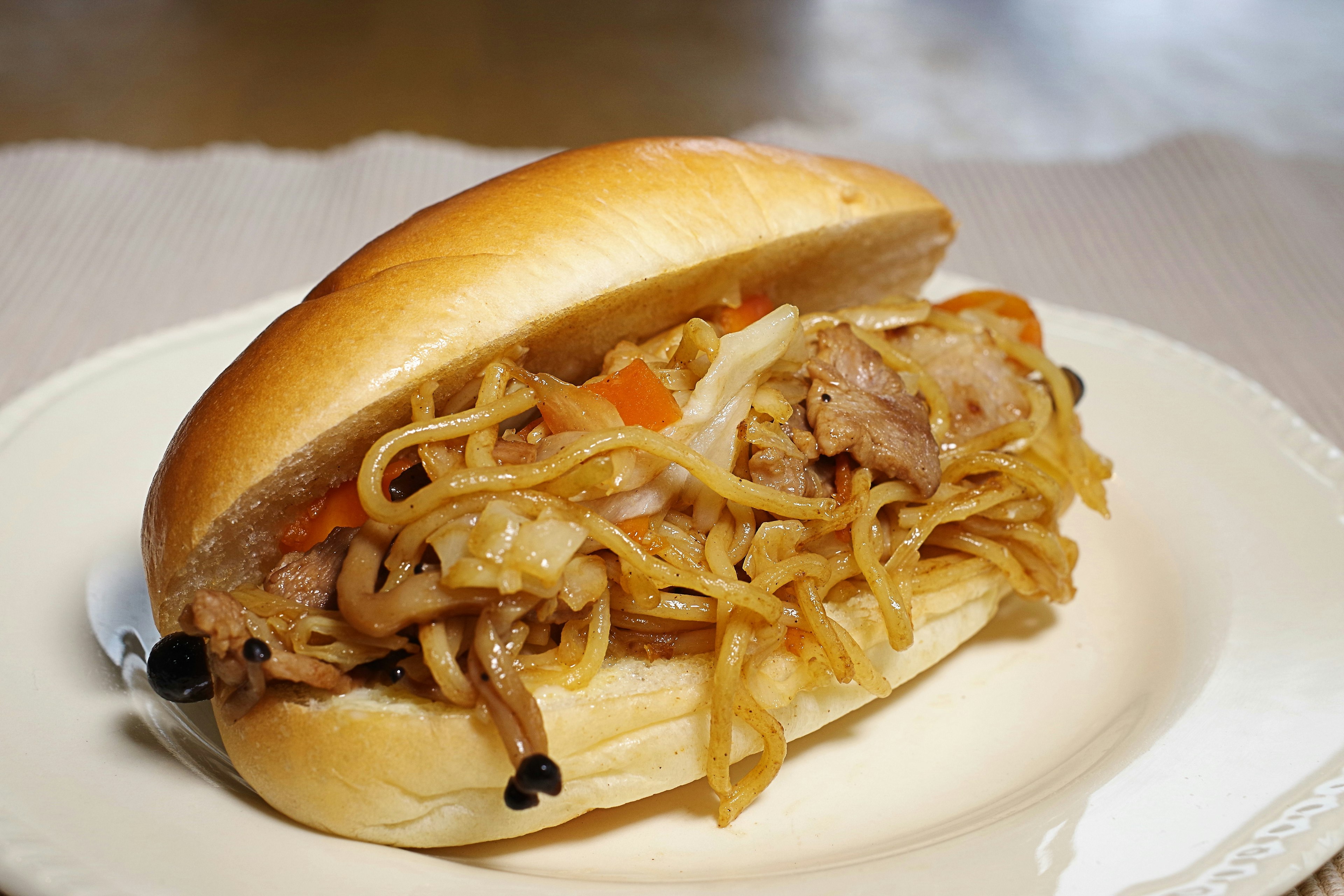 Noodle-filled sandwich with vegetables and meat in a soft bun