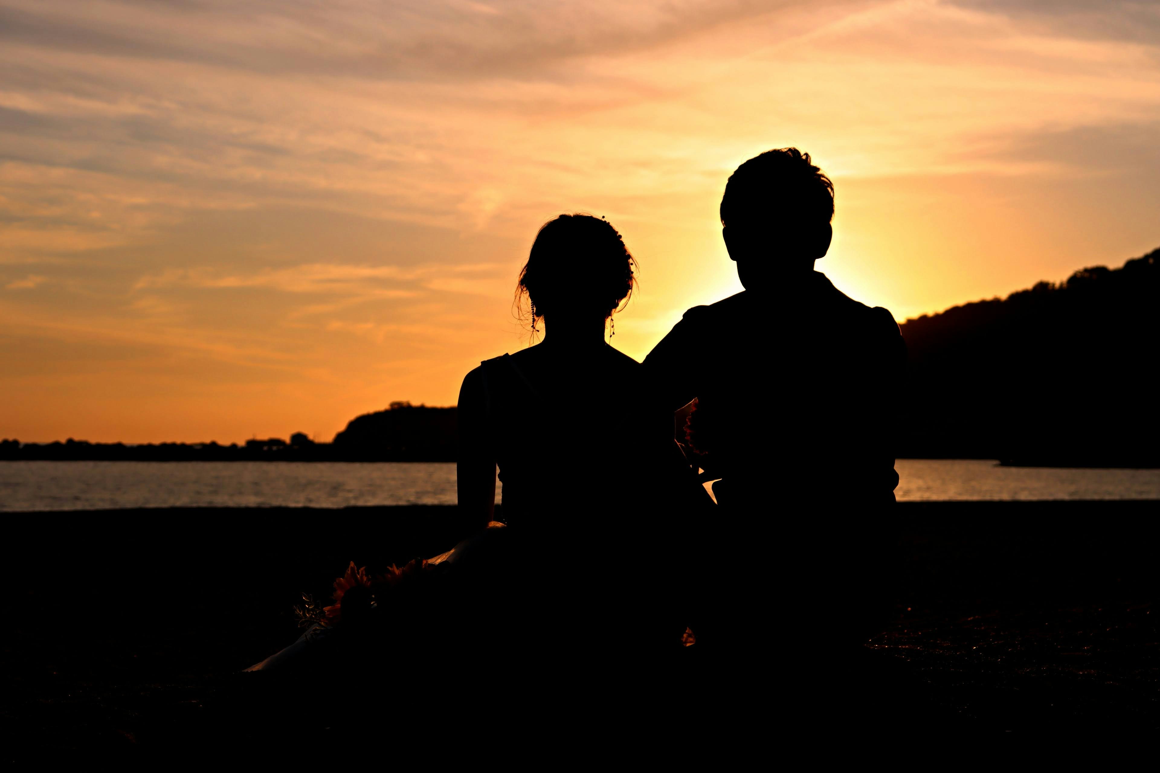 Silhouette of two people against a sunset by the beach