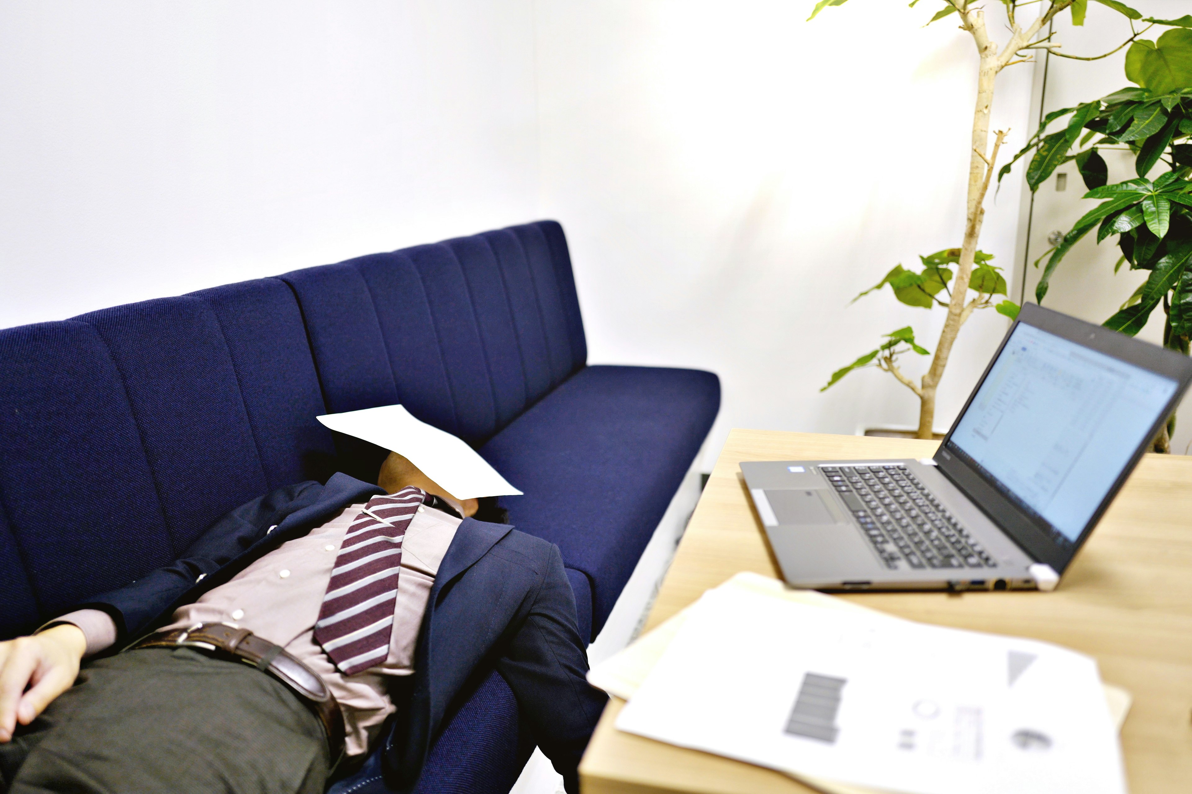 Geschäftsmann liegt auf einem blauen Sofa mit einem Laptop in der Nähe