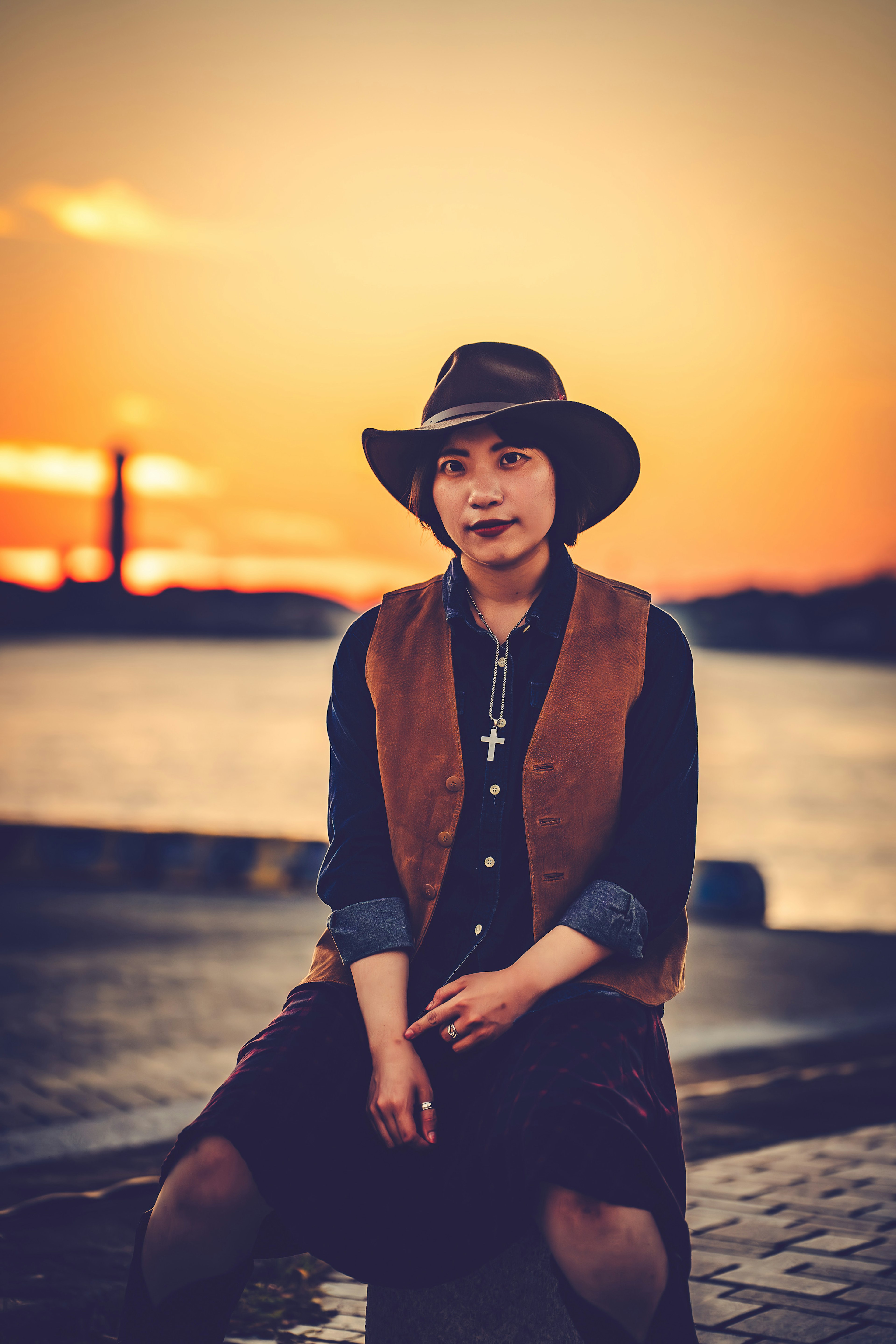 Portrait of a woman against a sunset wearing a hat and vest sitting with a serene expression