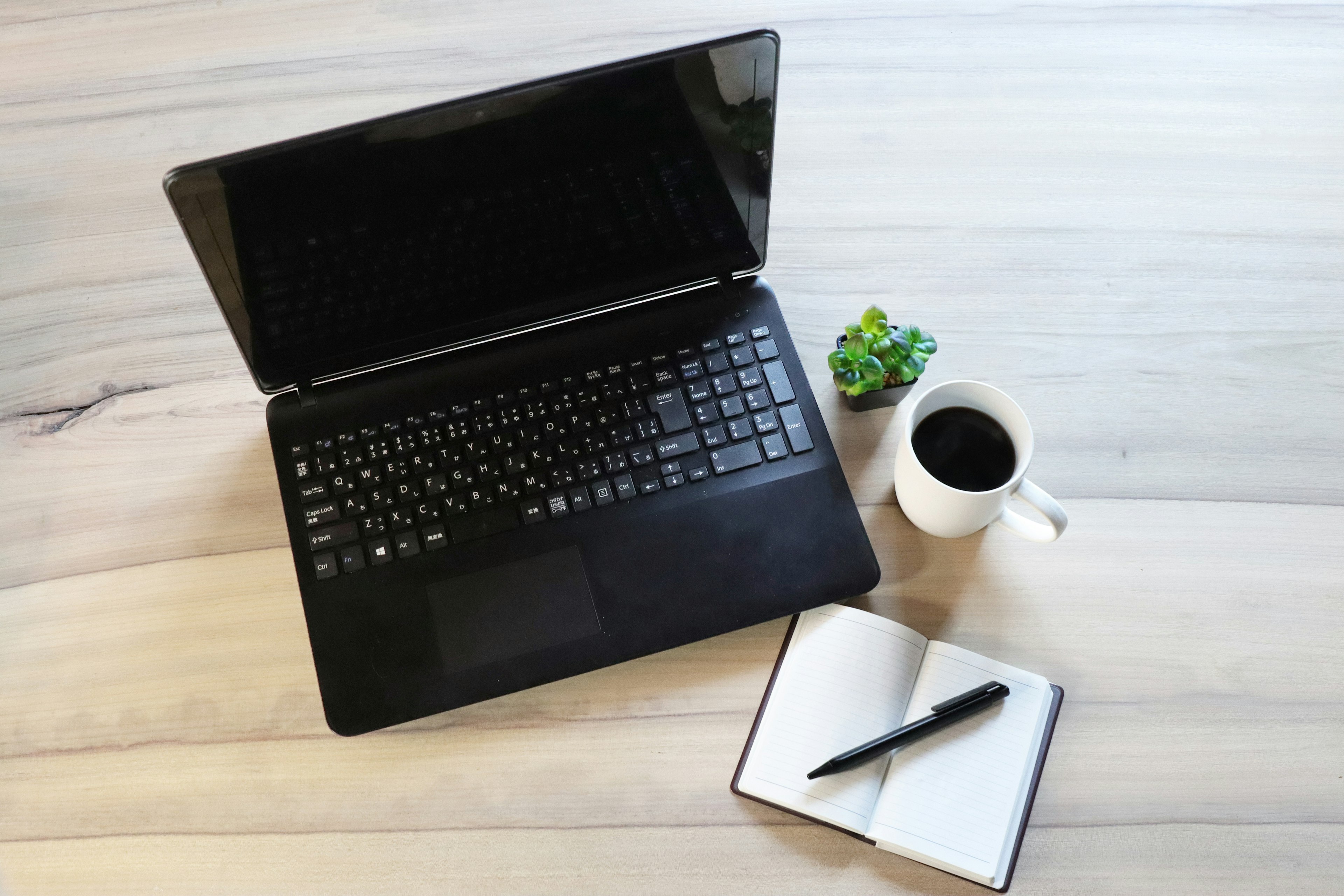 Una laptop negra con una taza de café y un cuaderno en un escritorio