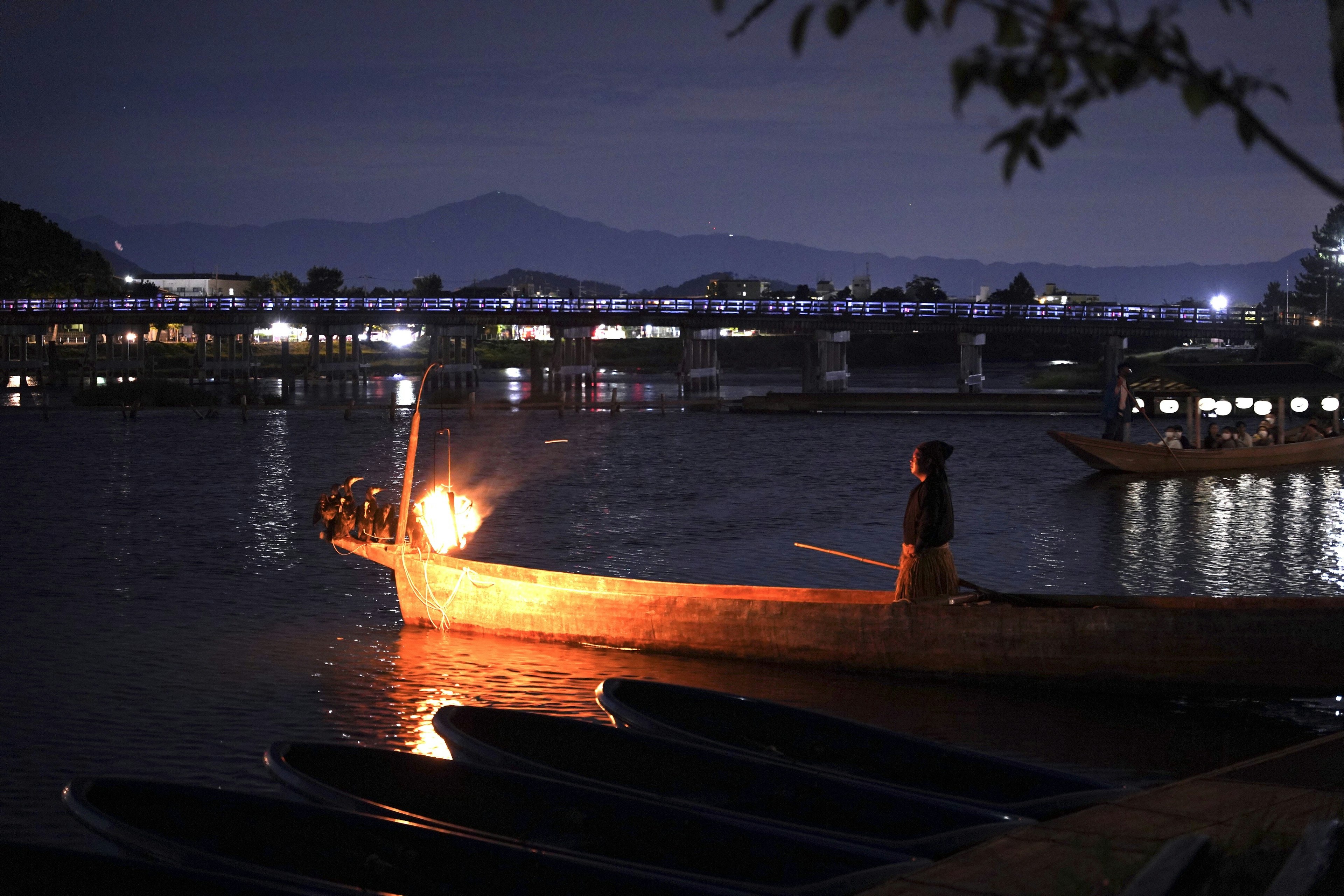 A small boat on a lake at night with silhouettes of nearby fishing boats