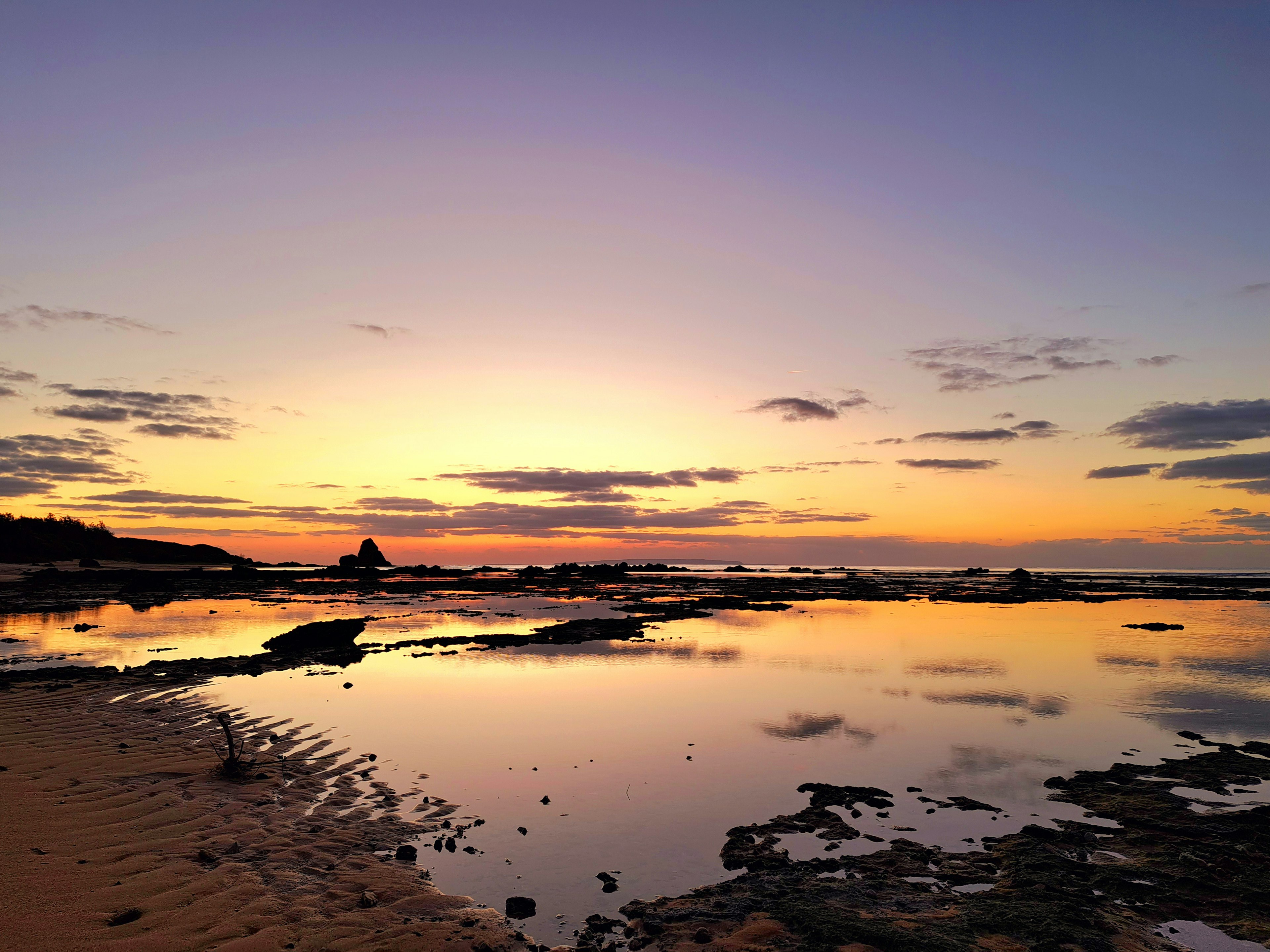 Bellissimo paesaggio costiero con riflessi del tramonto che brillano sull'acqua e silhouette di rocce