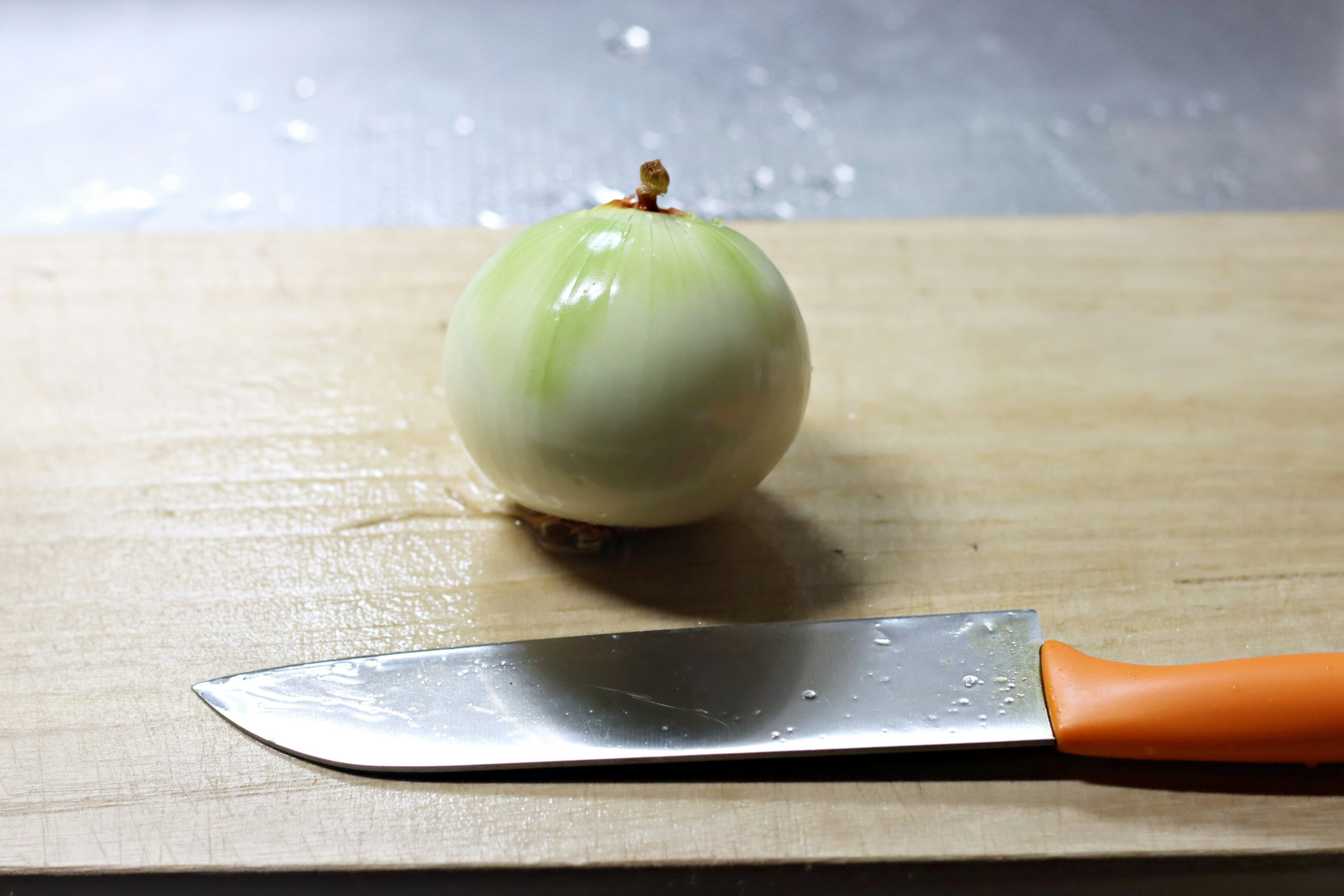 Una cebolla verde sobre una tabla de cortar de madera junto a un cuchillo de mango naranja