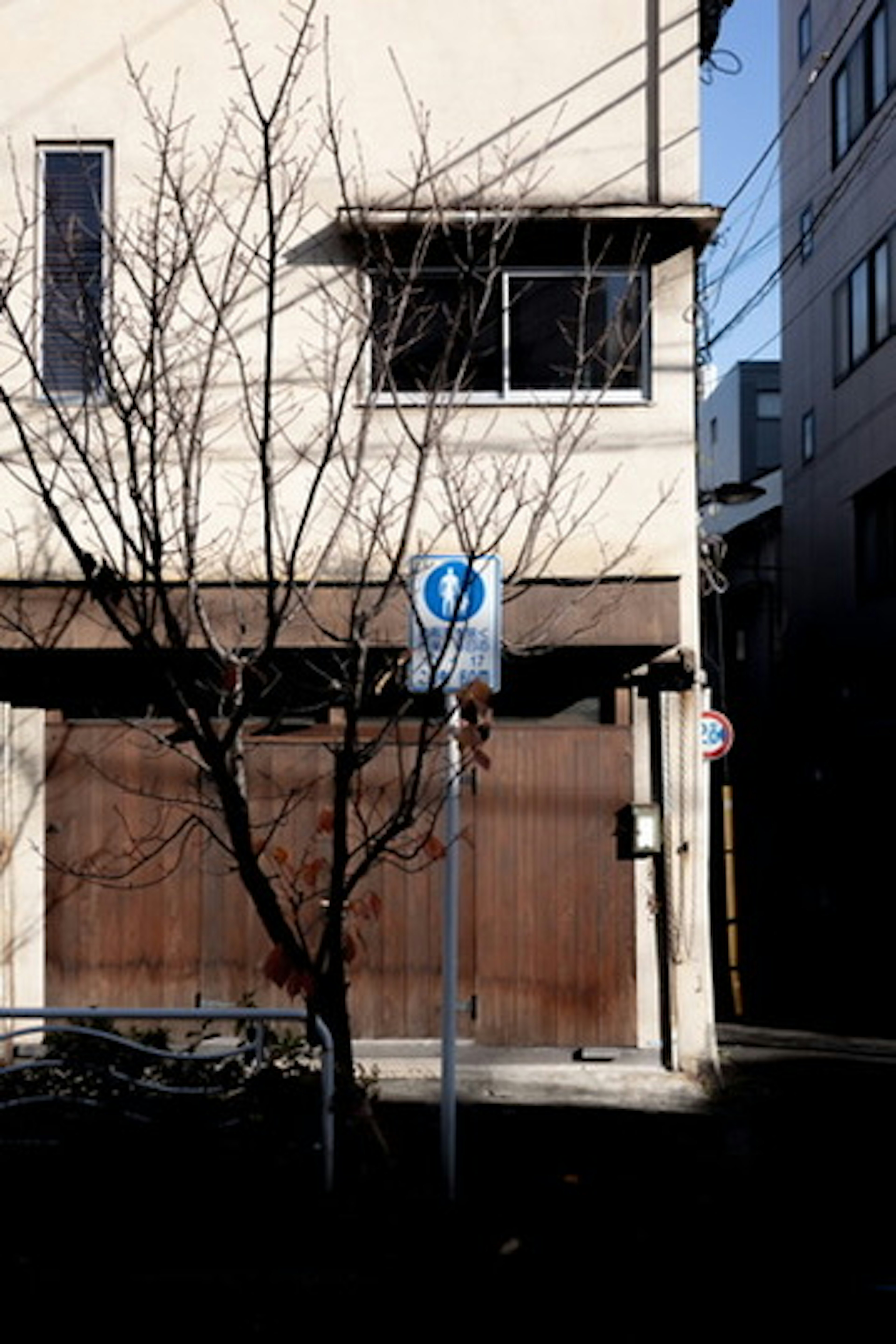 Panneau d'arrêt de bus devant une vieille maison avec un arbre nu