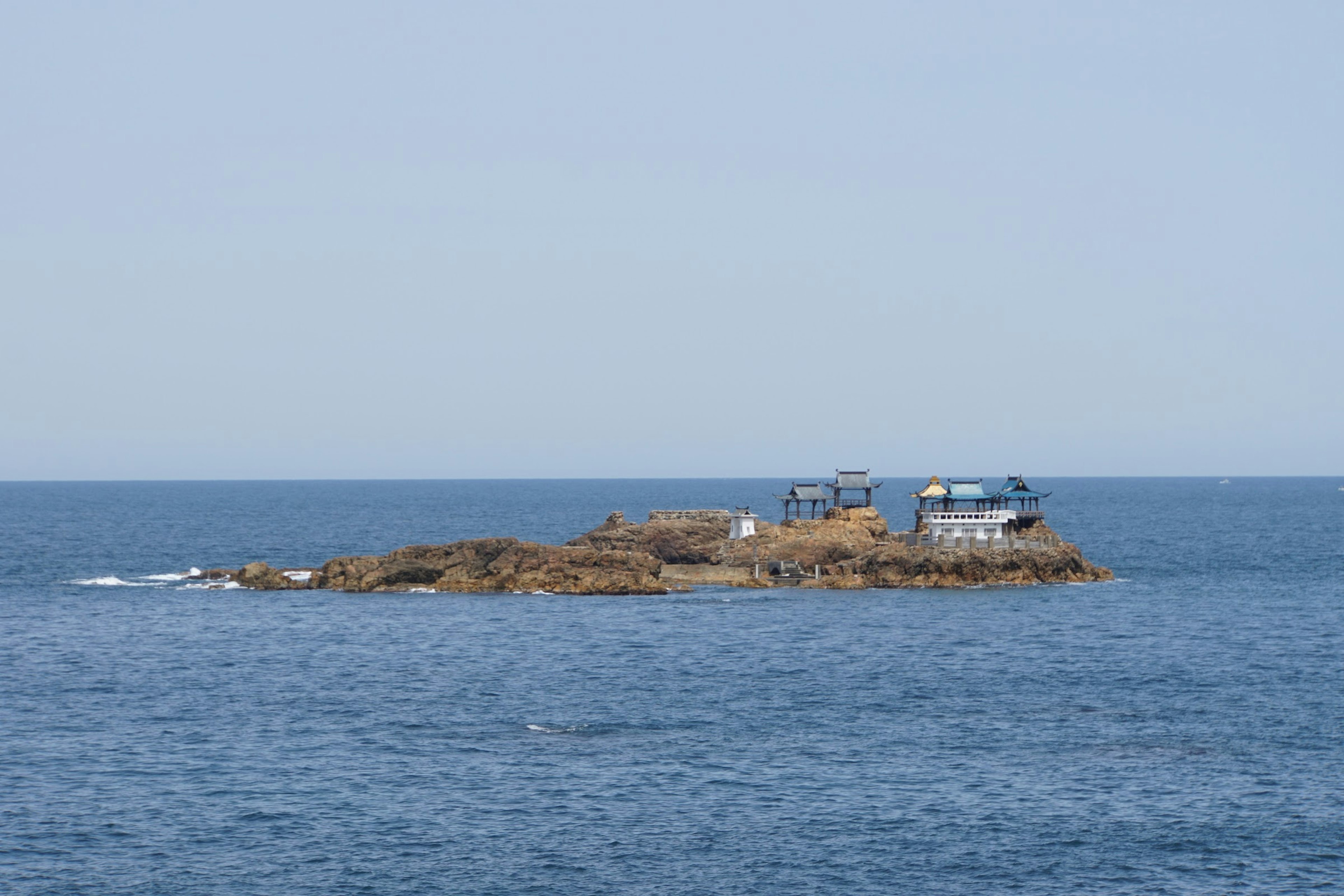 Une petite île entourée par la mer bleue avec des bâtiments dessus