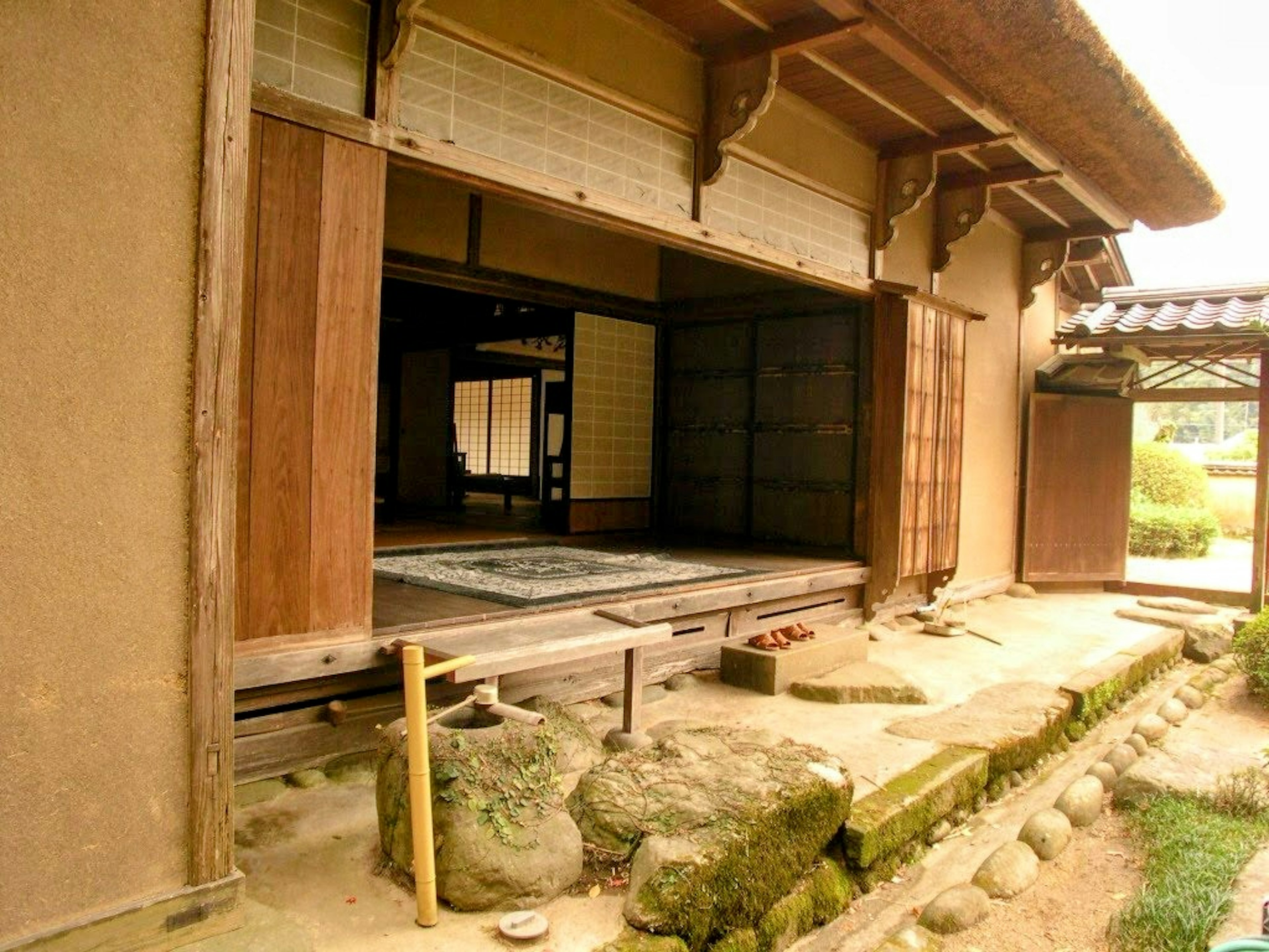 Außenansicht eines traditionellen japanischen Hauses mit Holztüren und Lehmwänden, die zum Garten geöffnet sind