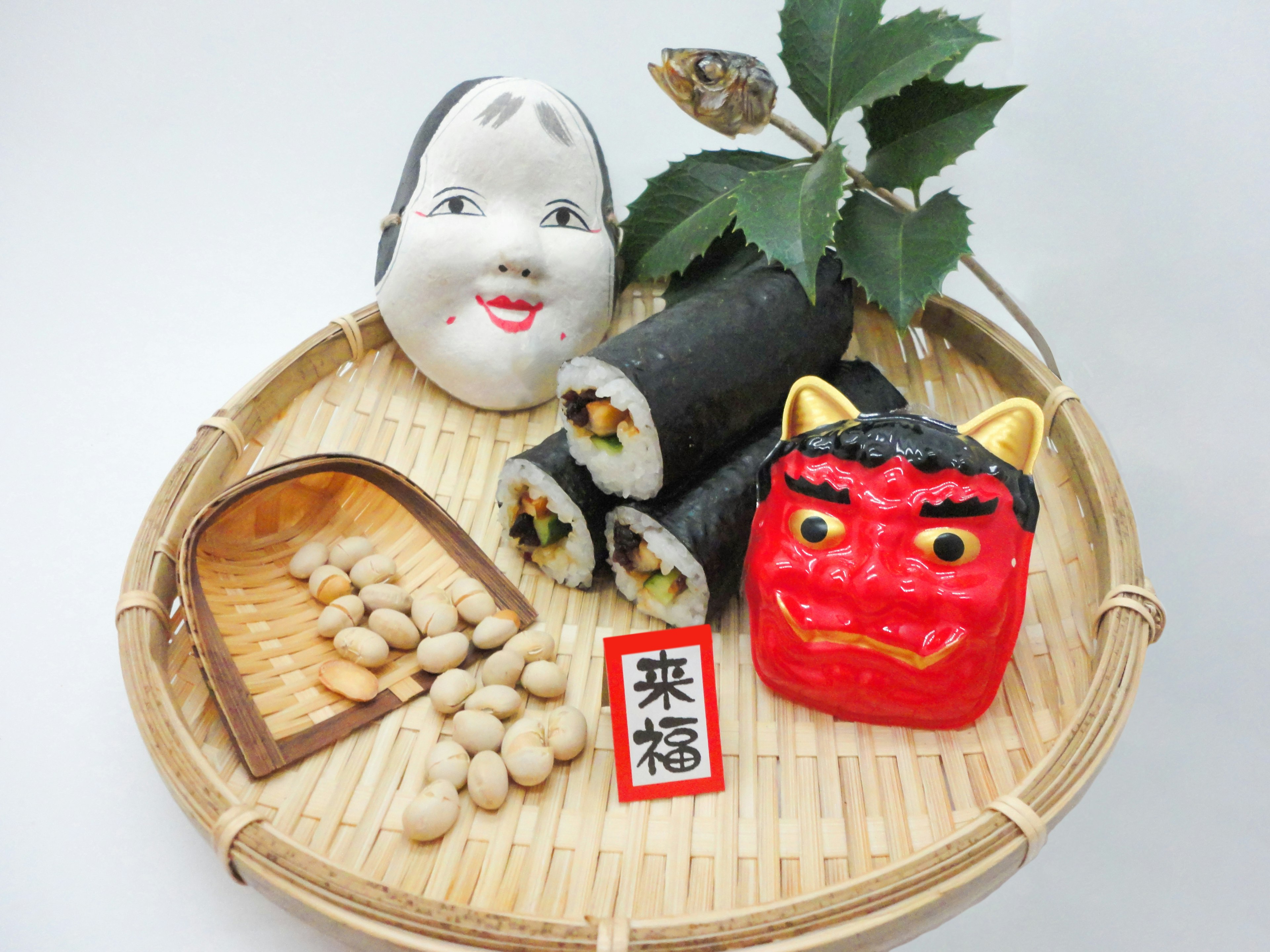 A plate featuring sushi rolls, beans, a demon mask, a smiling doll, and decorative leaves