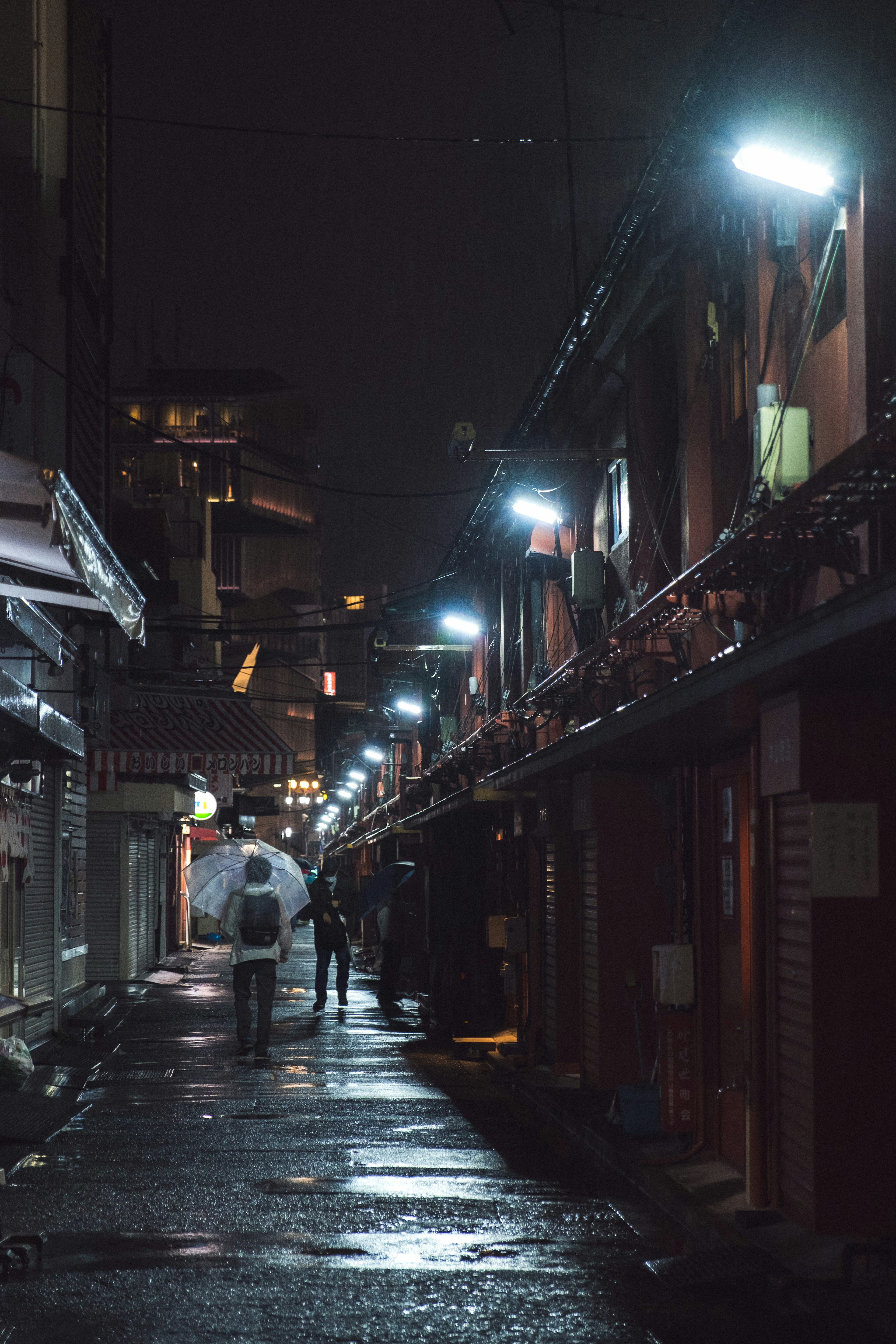 Narrow street at night with people holding umbrellas and bright streetlights