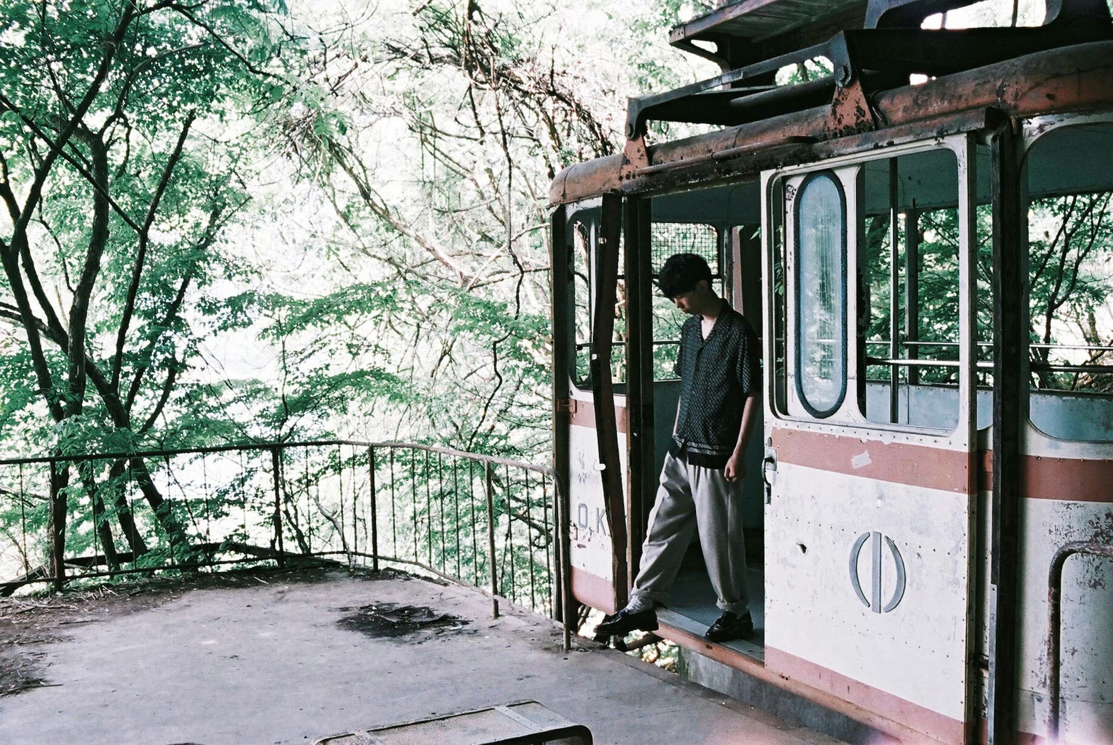 A man standing at an old cable car station surrounded by green trees