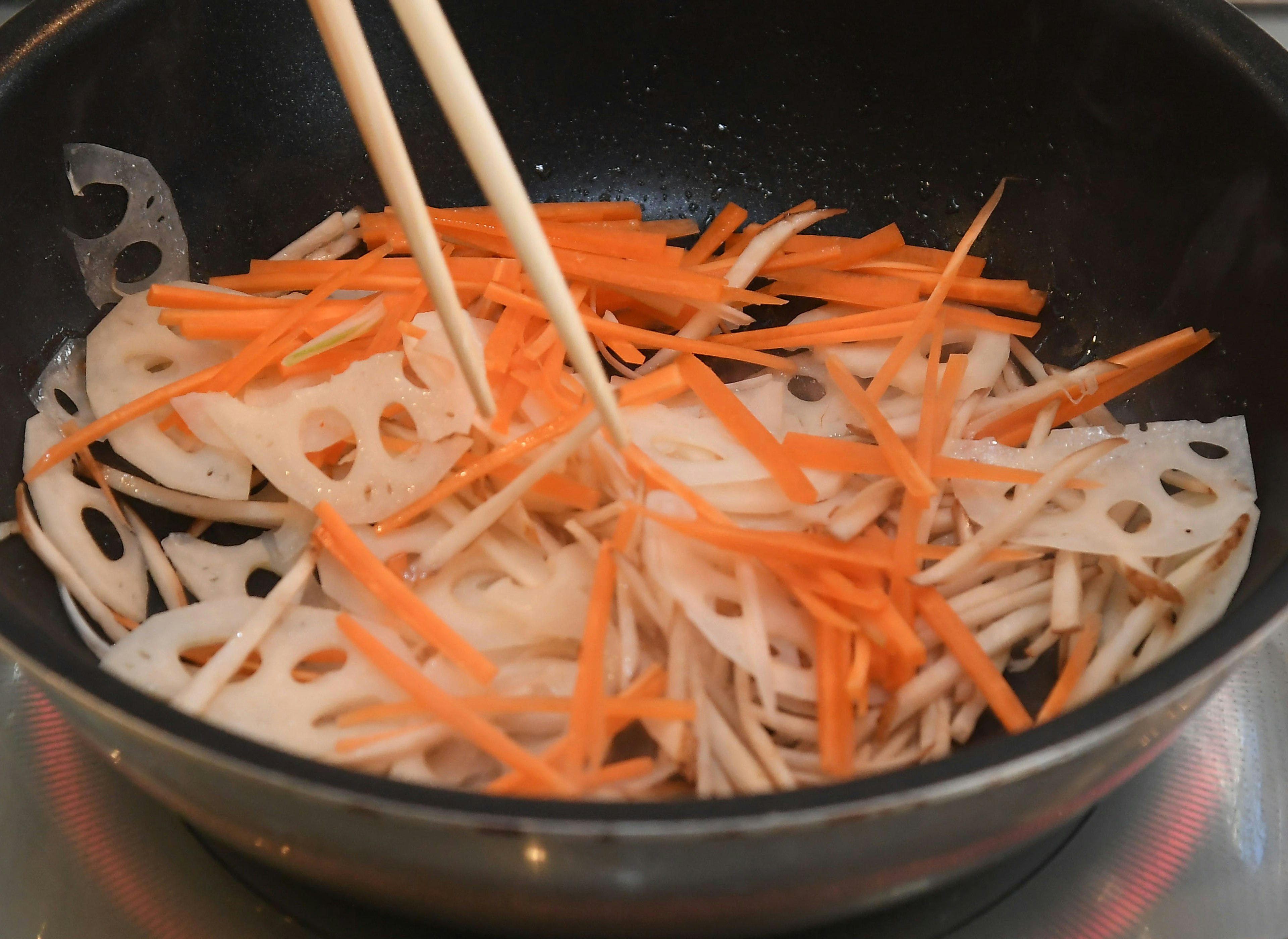 Sliced lotus root and carrots being cooked in a pot