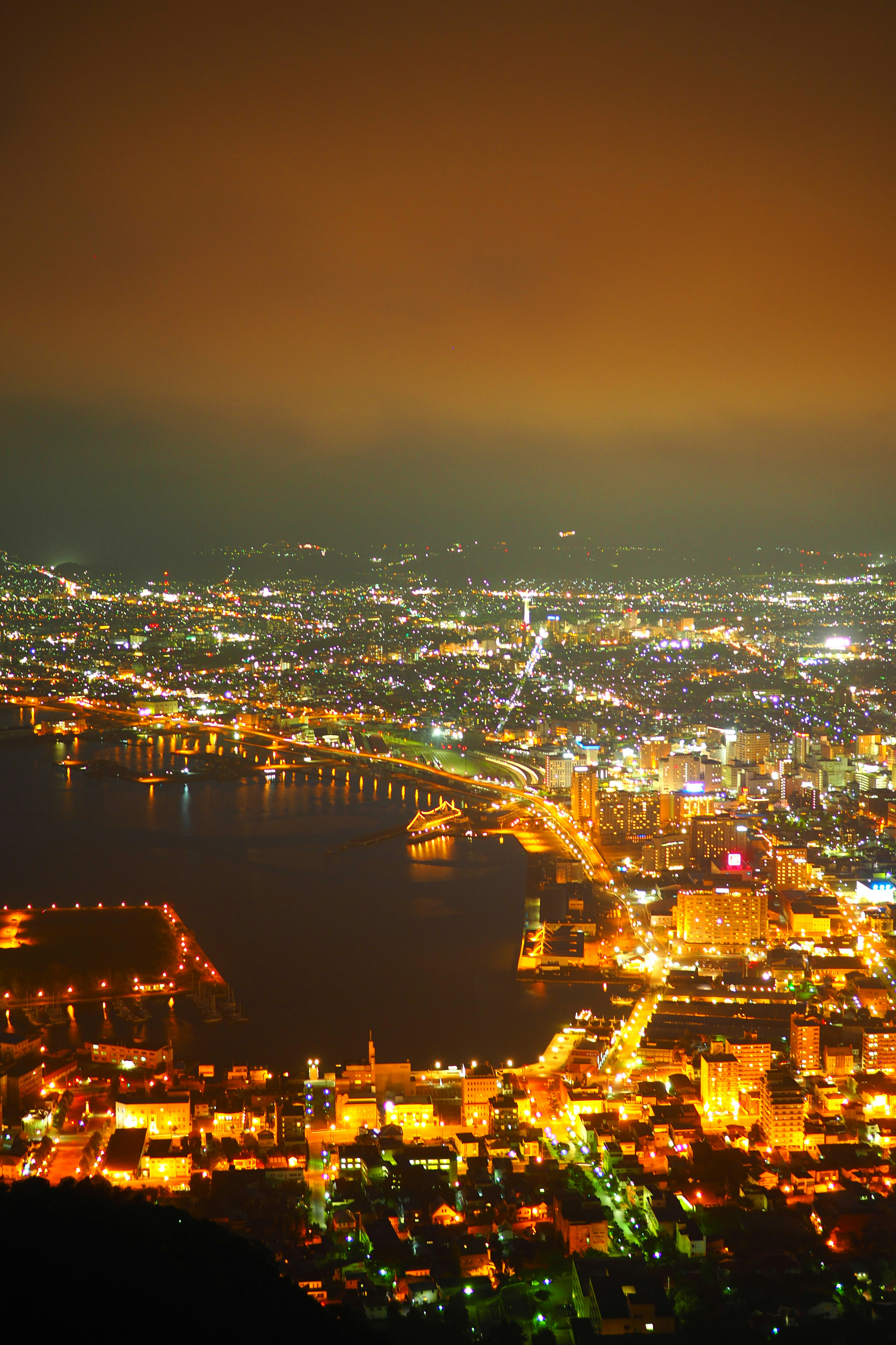 Panoramic view of a beautiful city at night featuring a harbor and bright streetlights