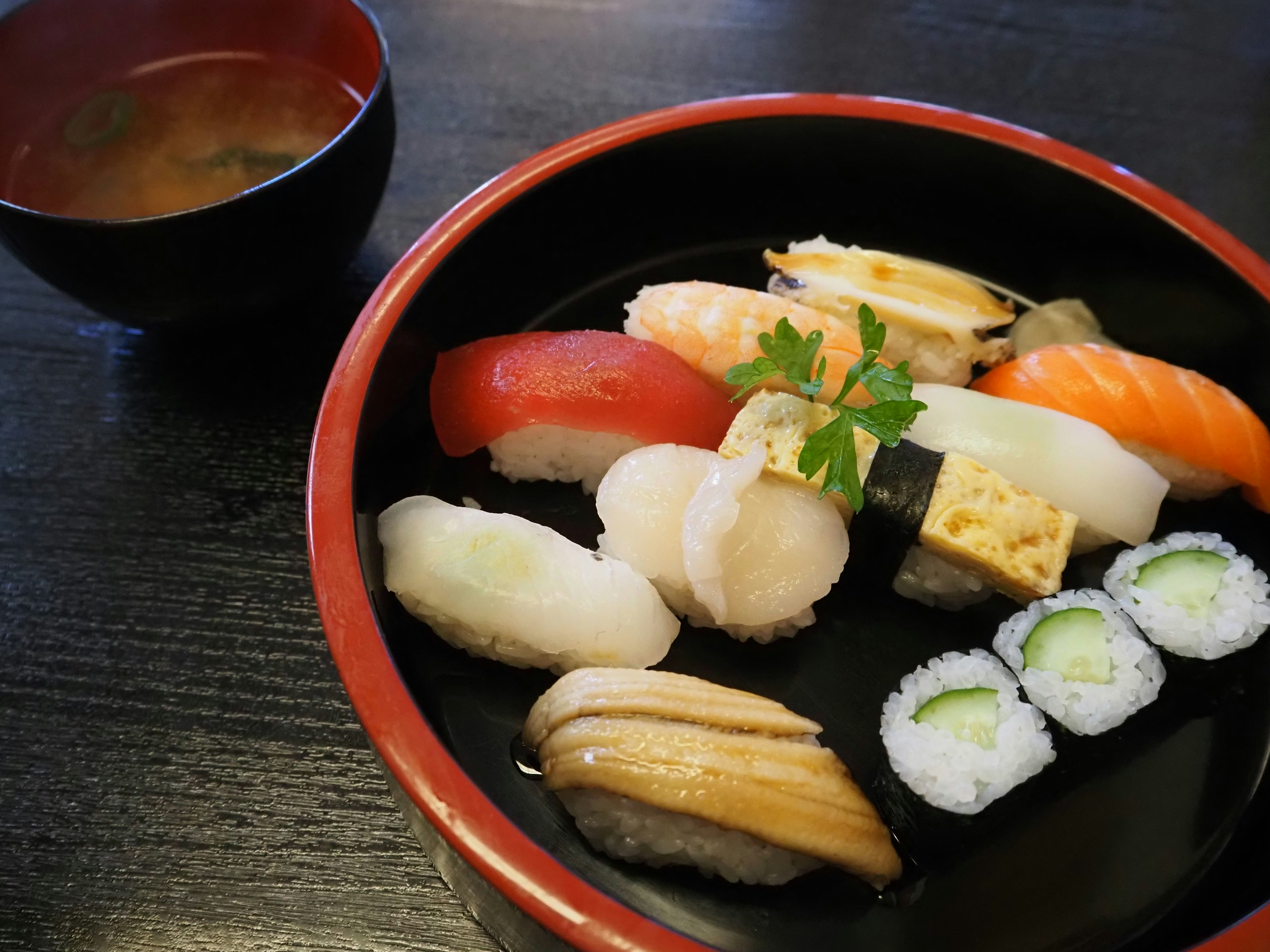 Image de sushi disposé sur une assiette rouge avec de la soupe miso