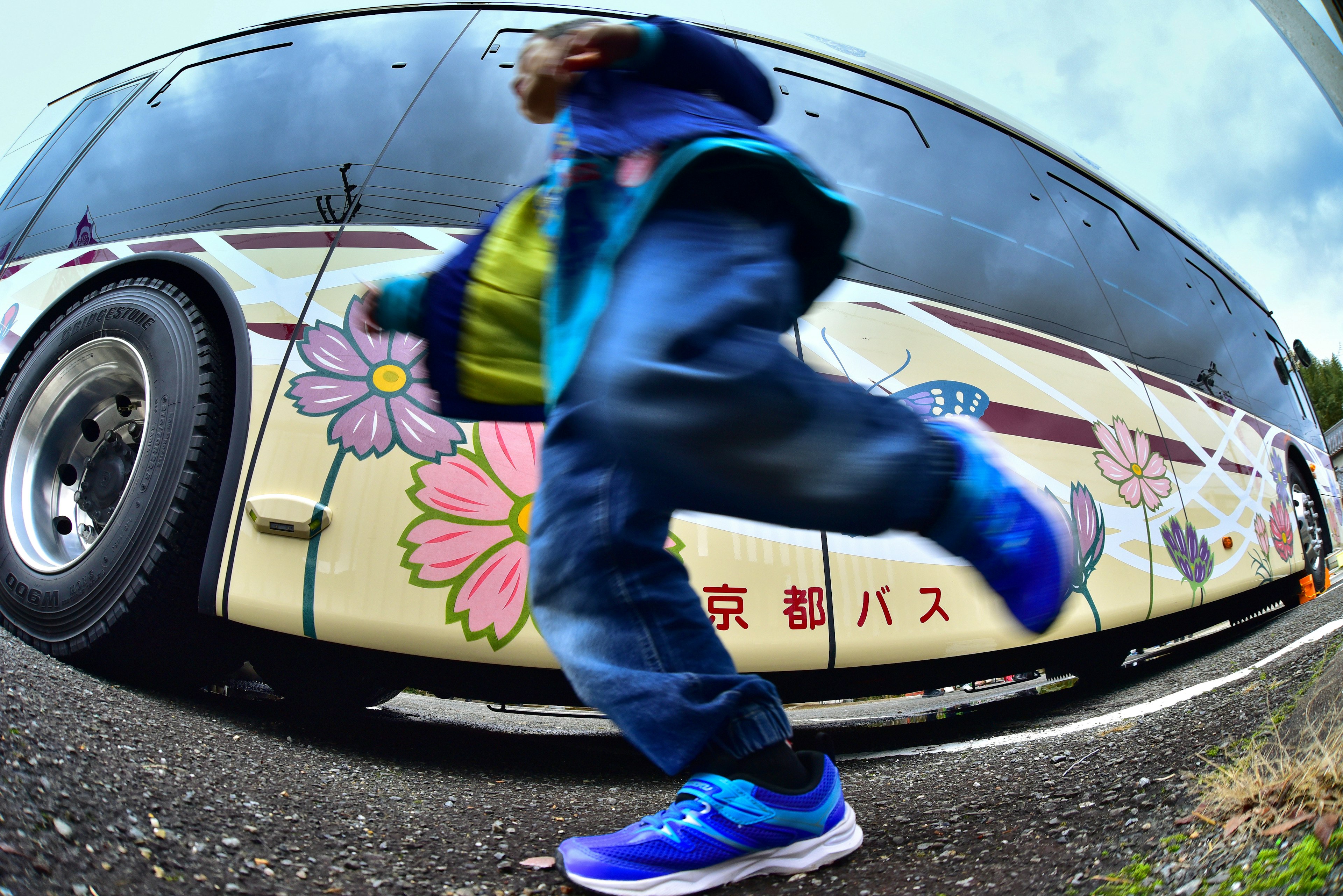 A child running beside a bus featuring floral designs and Japanese text