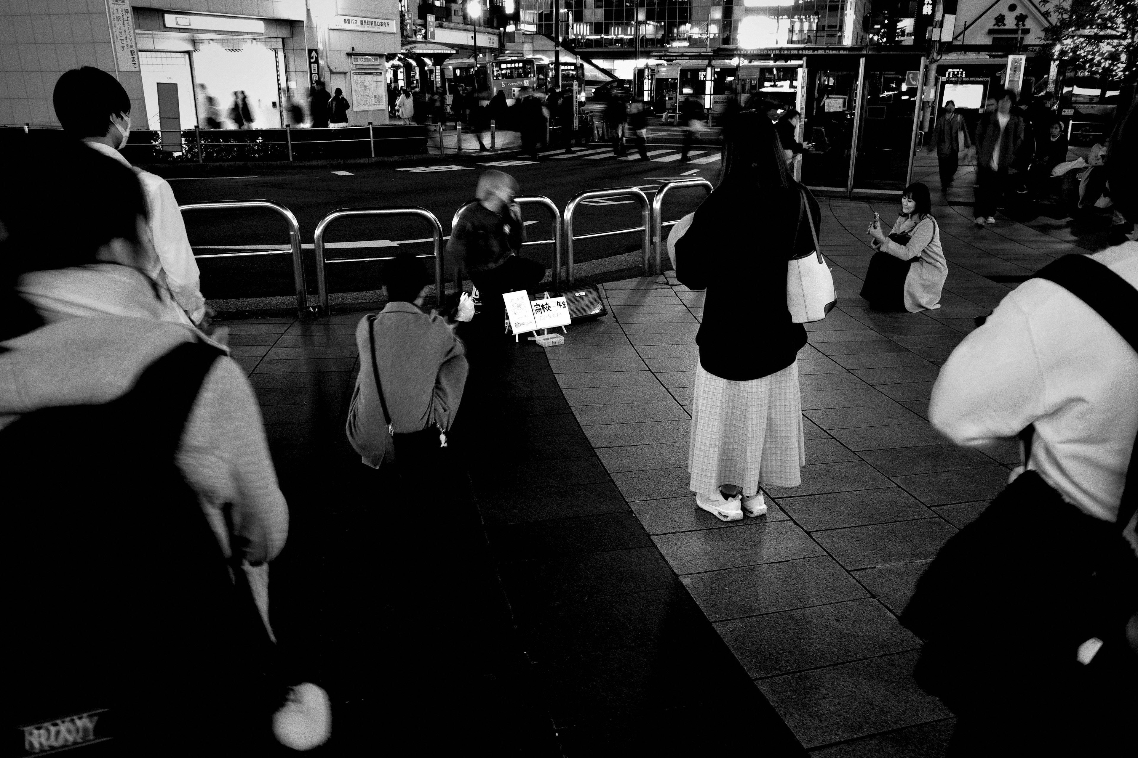 Schwarzweißfoto einer geschäftigen urbanen Szene bei Nacht mit versammelten Menschen