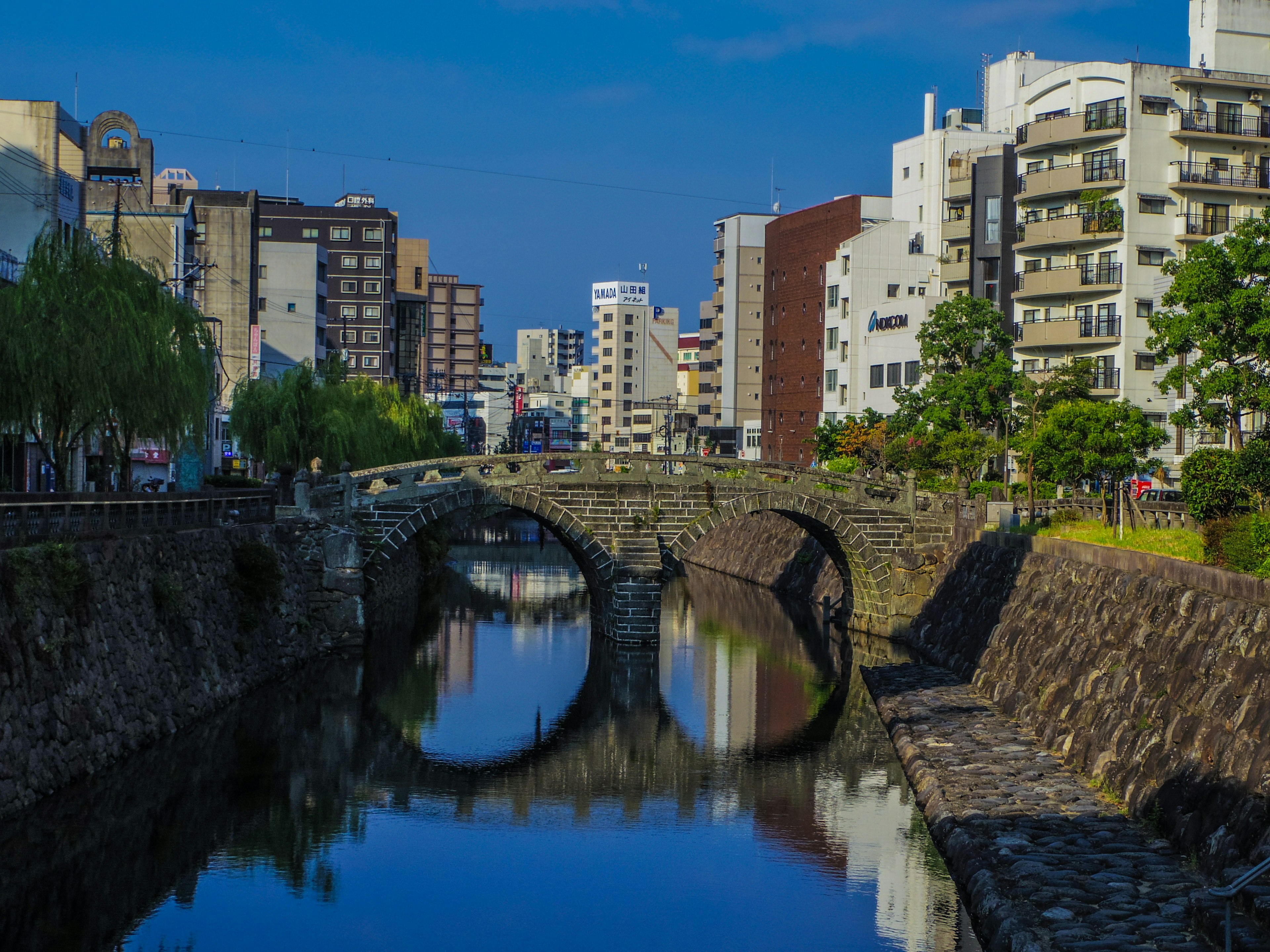 Una scena fluviale con un ponte in pietra sotto un cielo blu e edifici lungo le rive