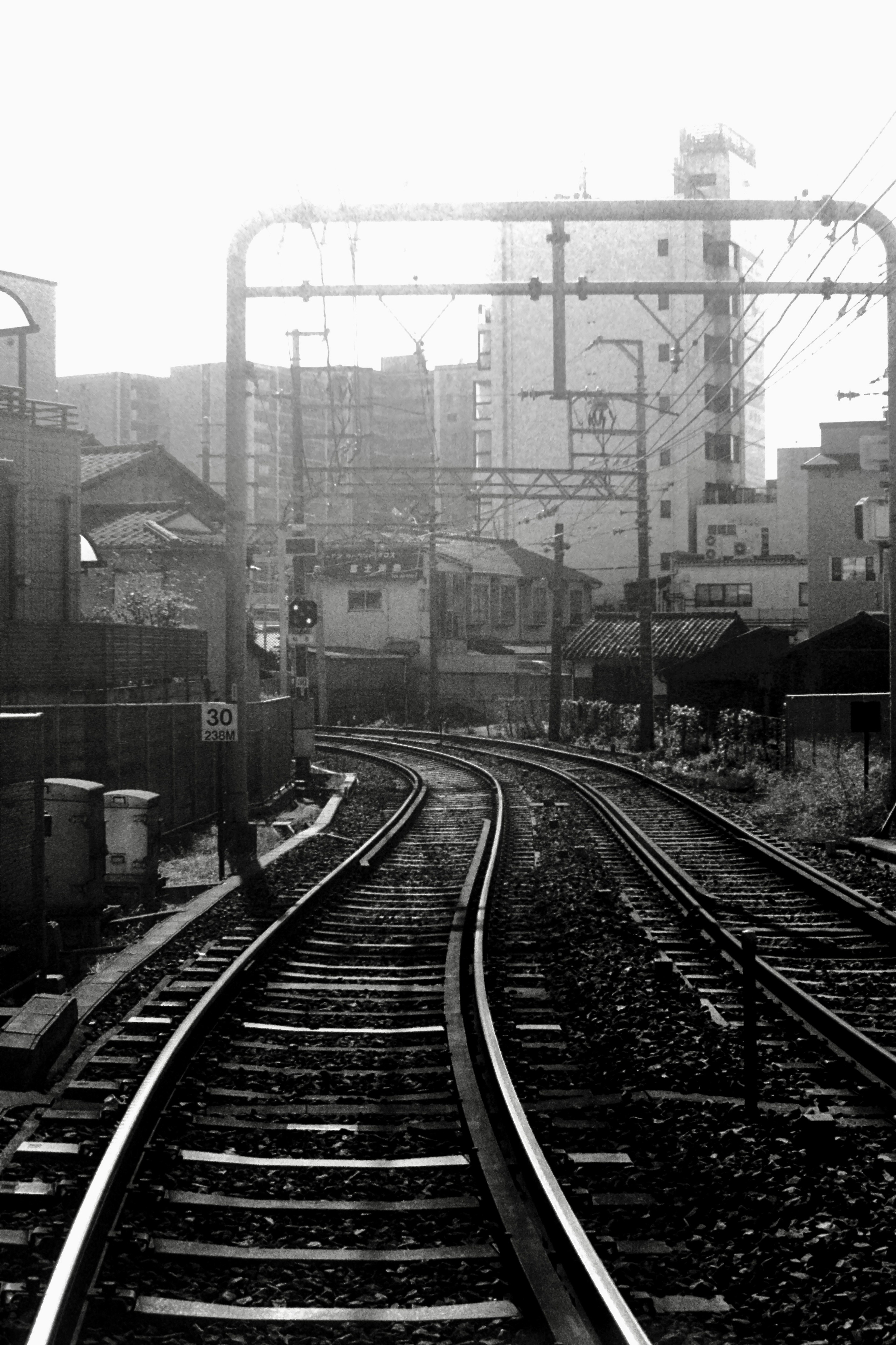 Vías de tren en blanco y negro que se curvan con edificios al fondo