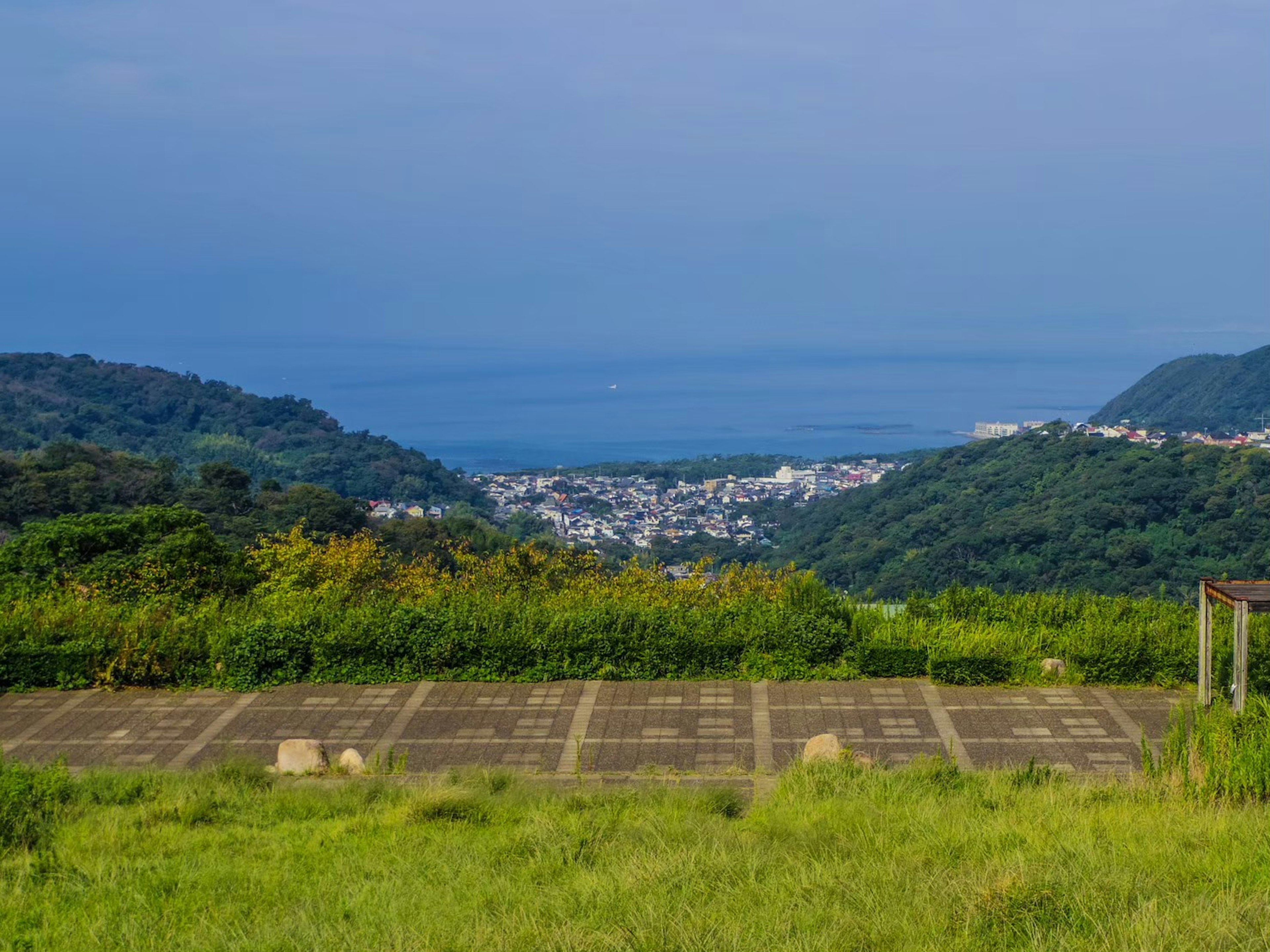 Aussicht von einem grünen Hügel auf das Meer und eine Stadt