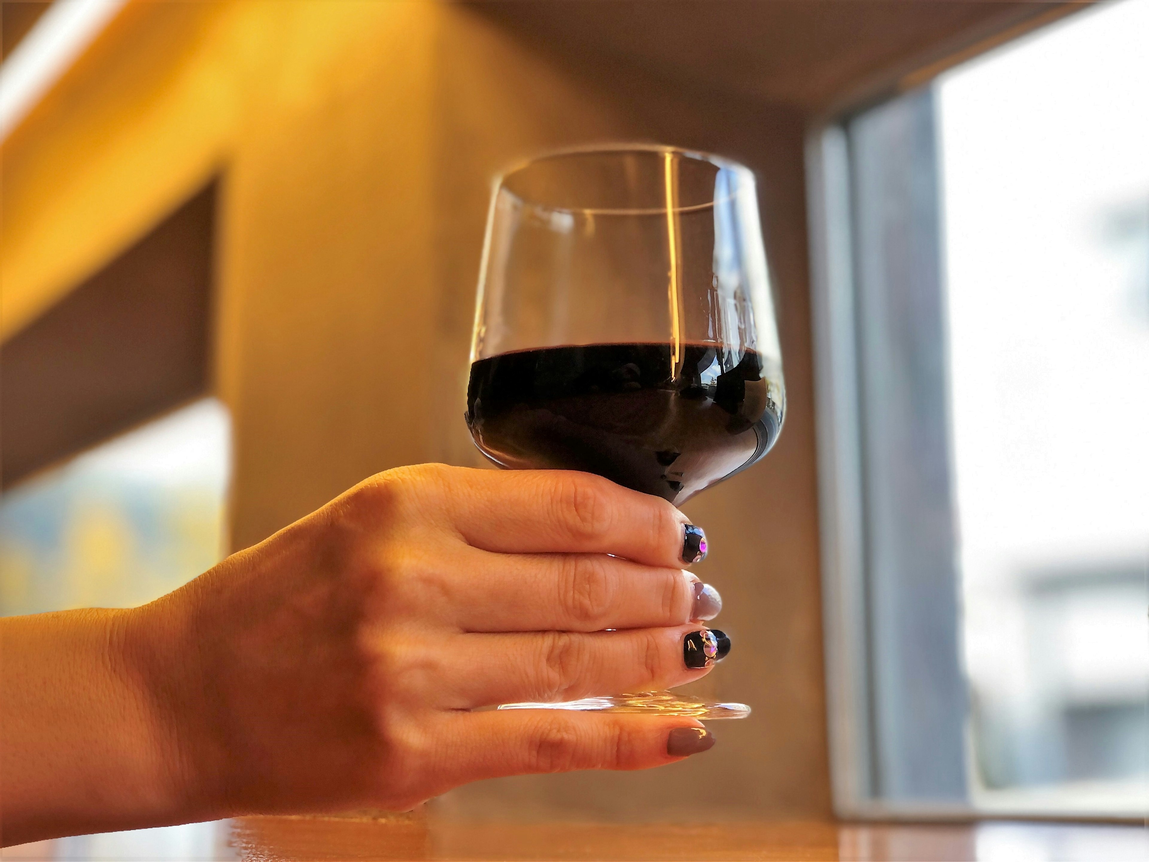 Eine Hand hält ein Glas Rotwein neben einem Fenster