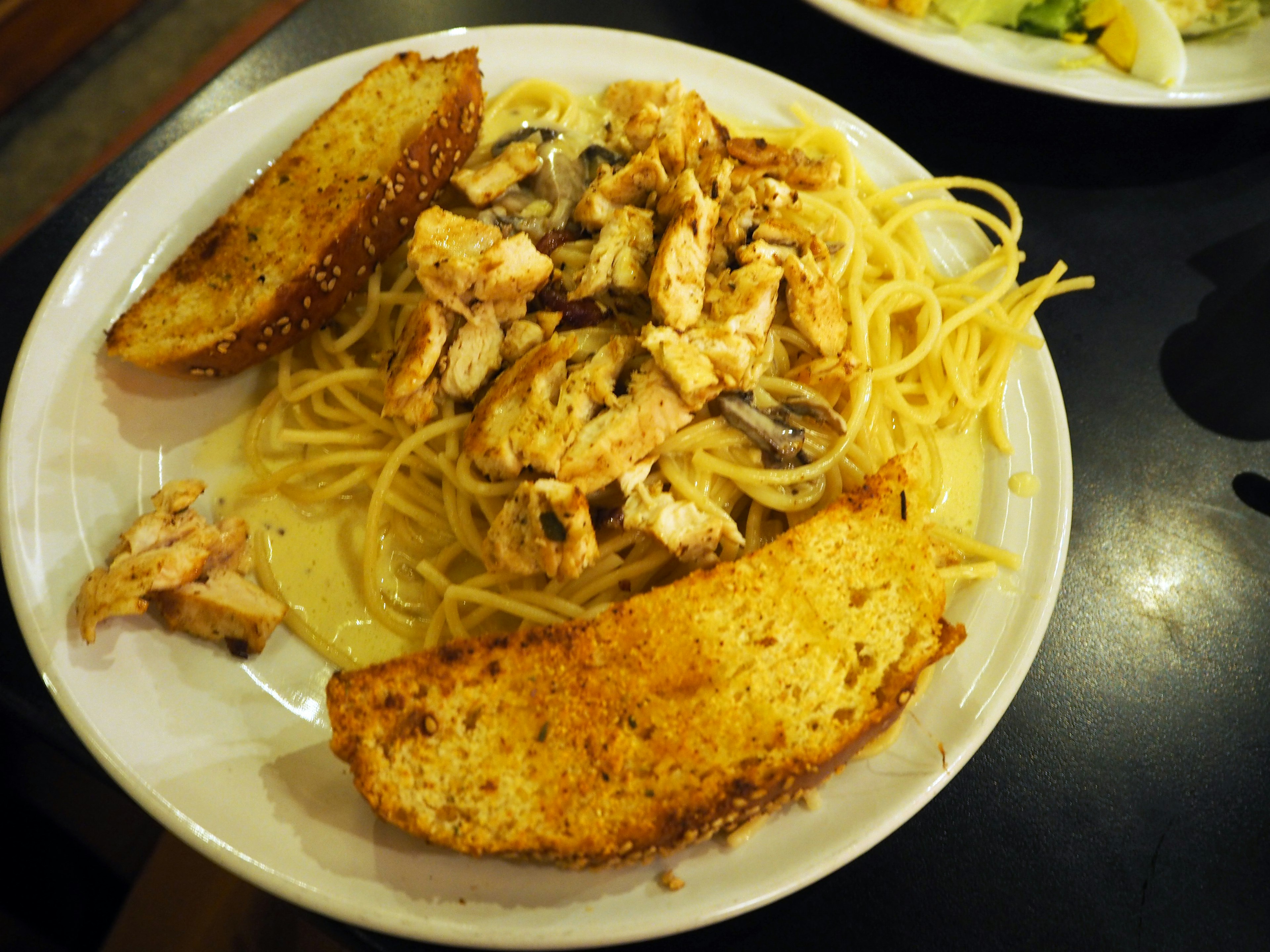 Cremige Hähnchenpasta mit Knoblauchbrot auf einem Teller