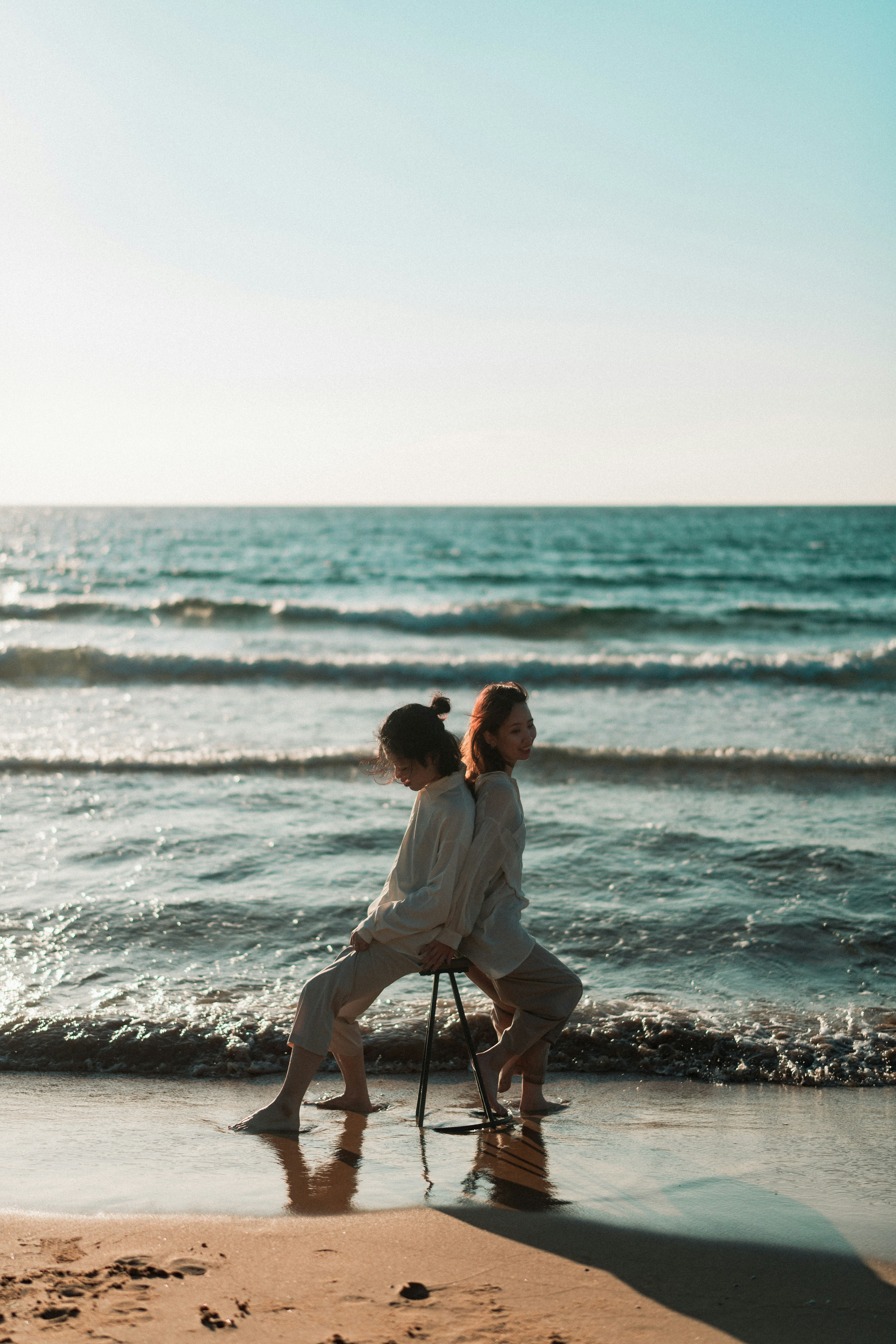 Two people sitting back to back on a chair by the beach