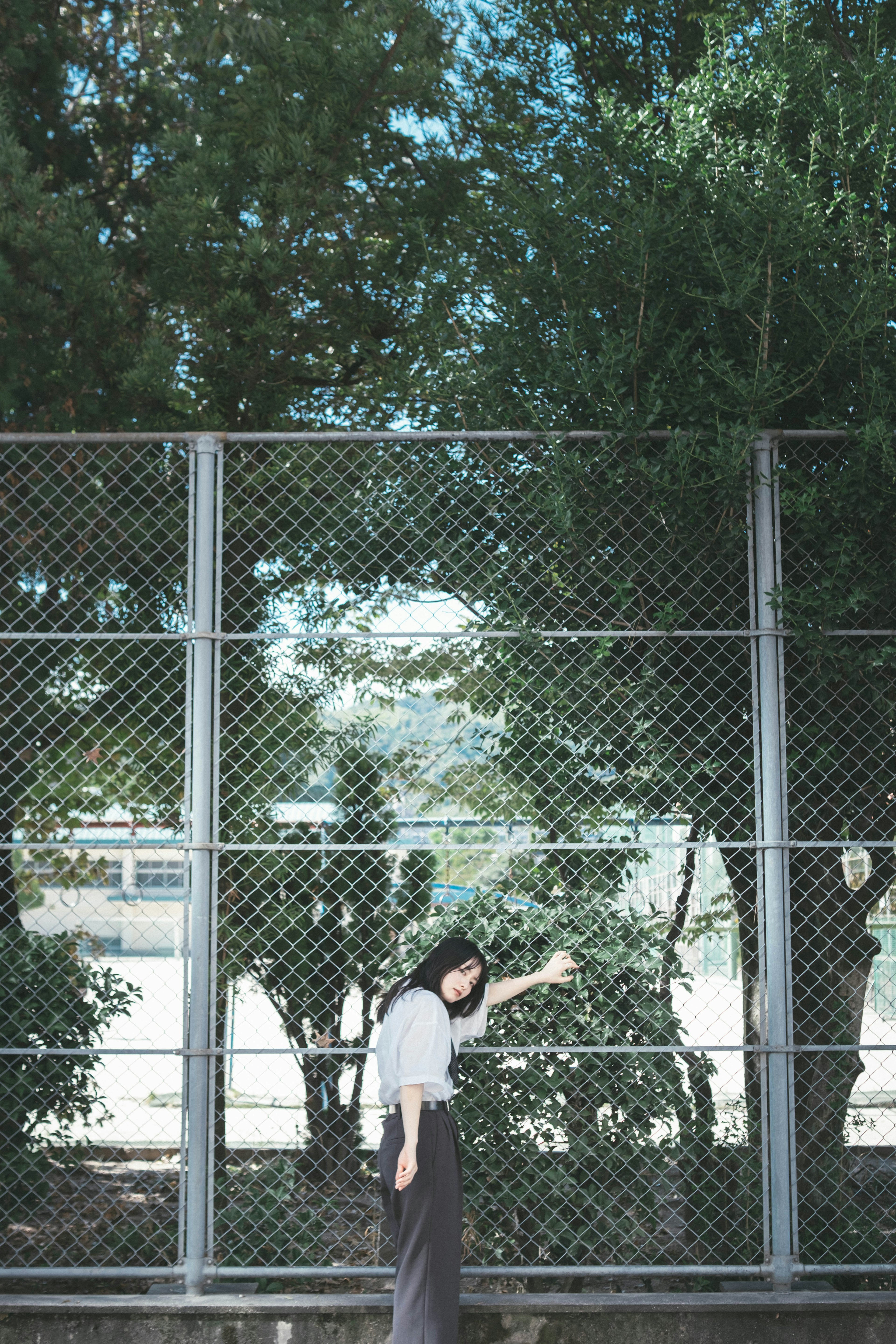 A woman reaching out towards a fence surrounded by trees