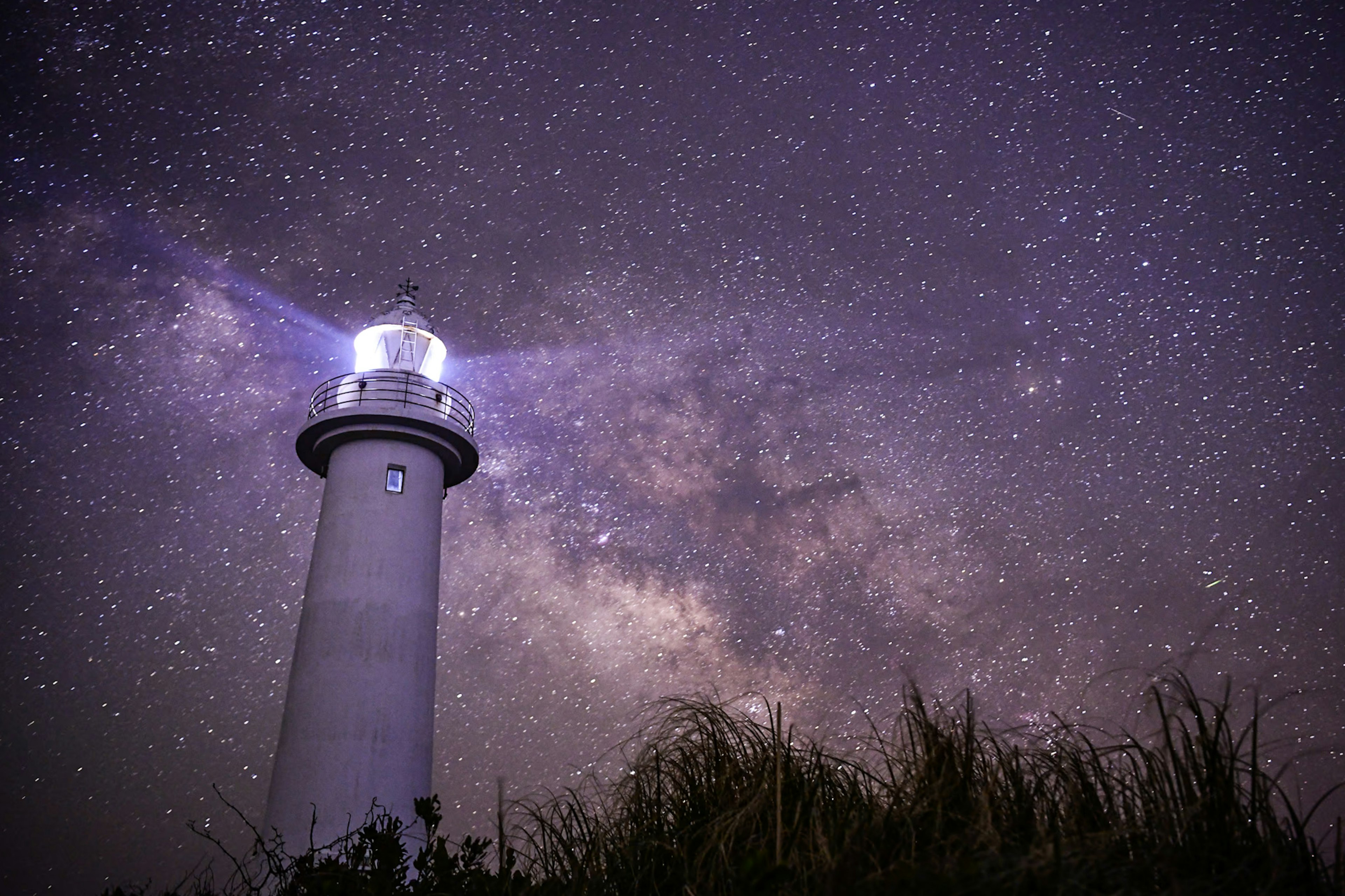 Un faro bajo un cielo estrellado con una vista impresionante de la Vía Láctea