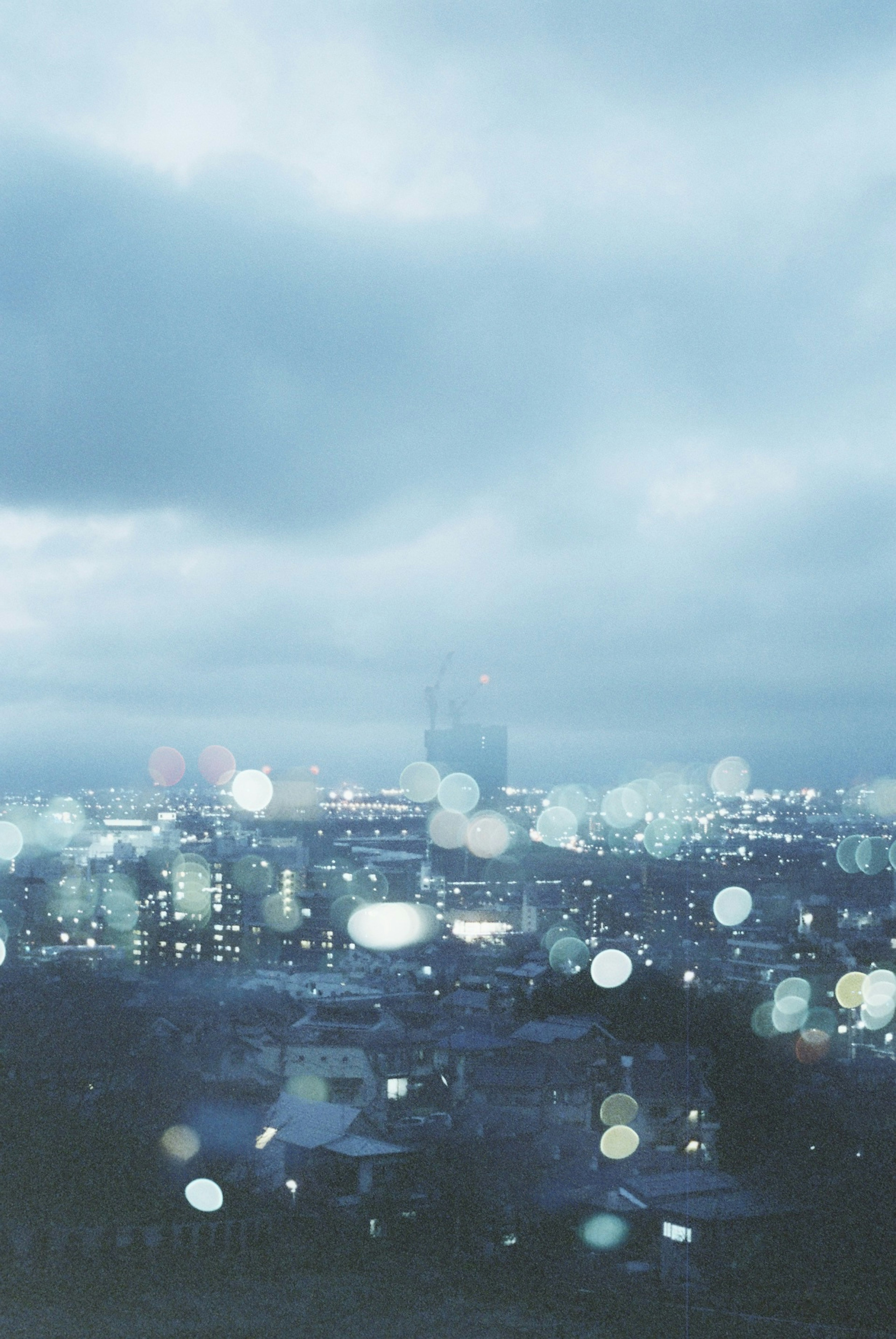 曇り空の下にある都市の夜景にぼやけた光が映る