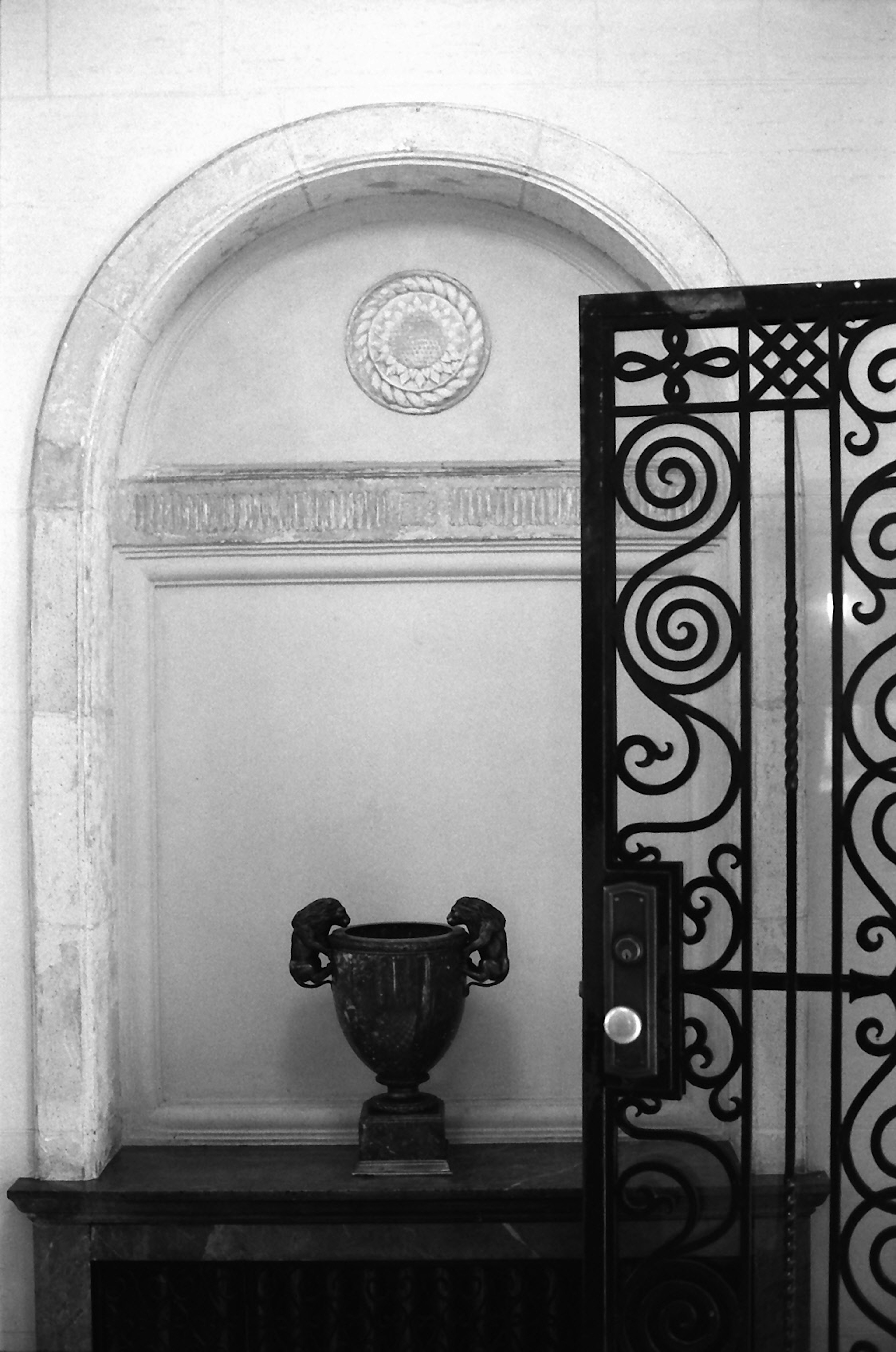 Puerta de hierro decorativa y jarrón clásico en una nicho arqueada sobre fondo blanco y negro