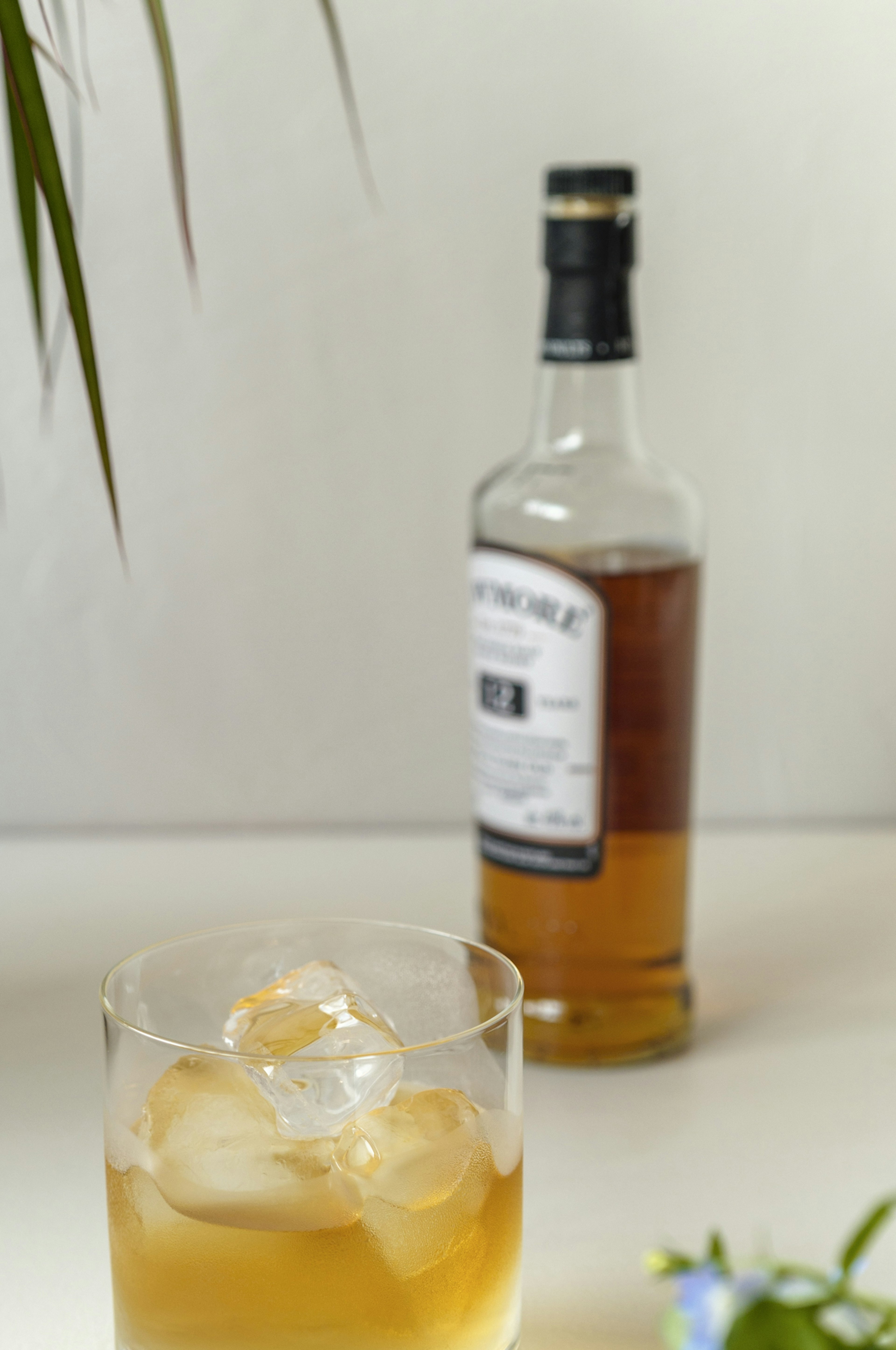 Glass with ice containing amber drink and bottle in the background