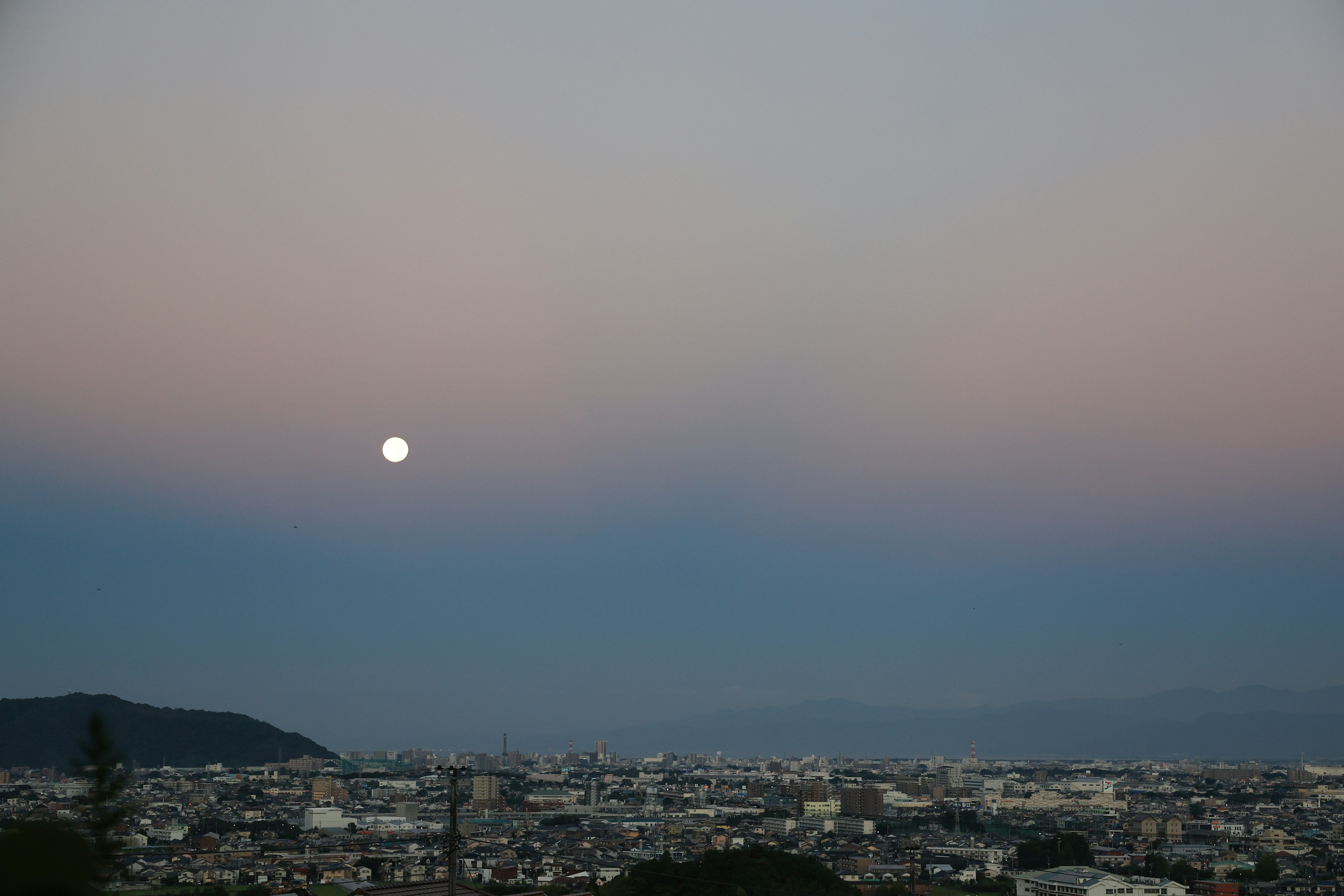 Full moon rising over a city landscape at dusk