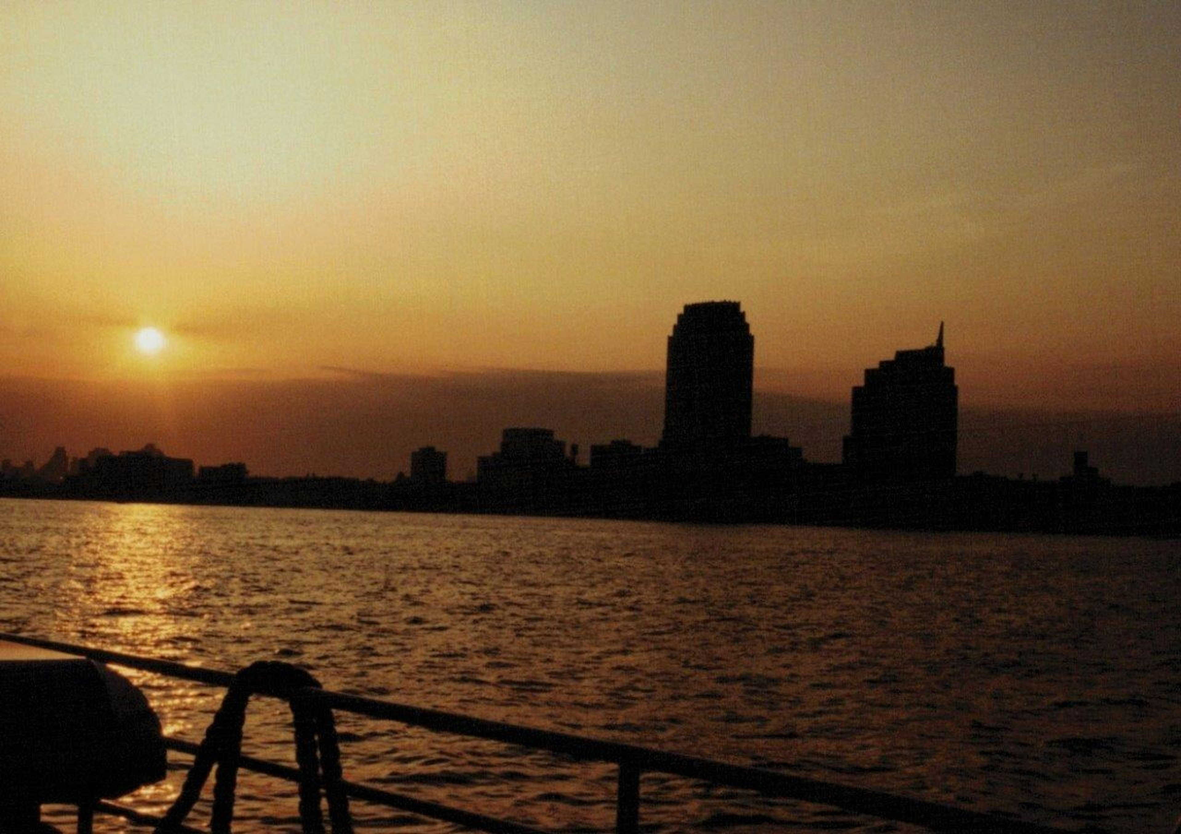 夕日が沈む都市のシルエットと水面の反射