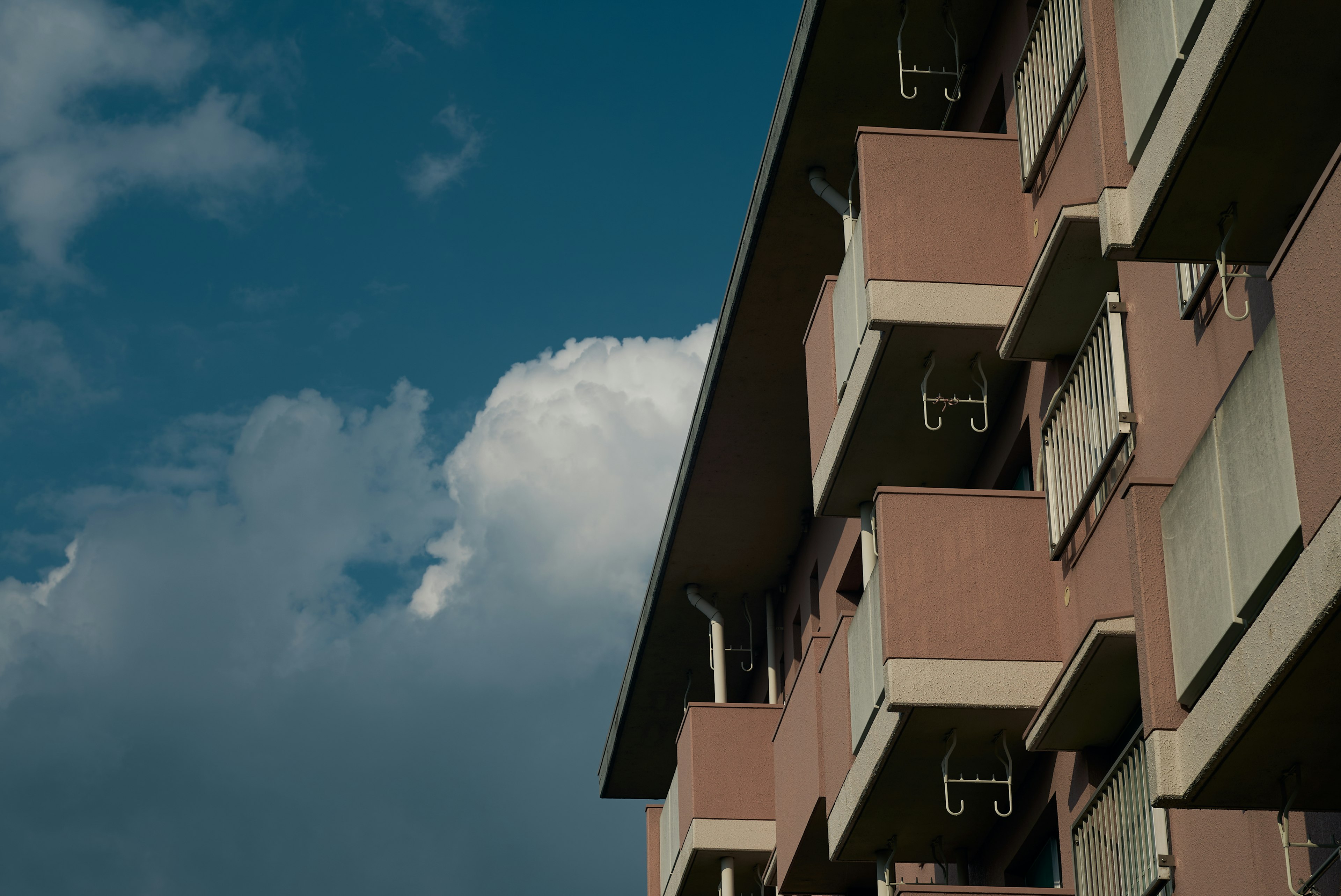 Bangunan apartemen berwarna pink dengan balkon di bawah langit biru