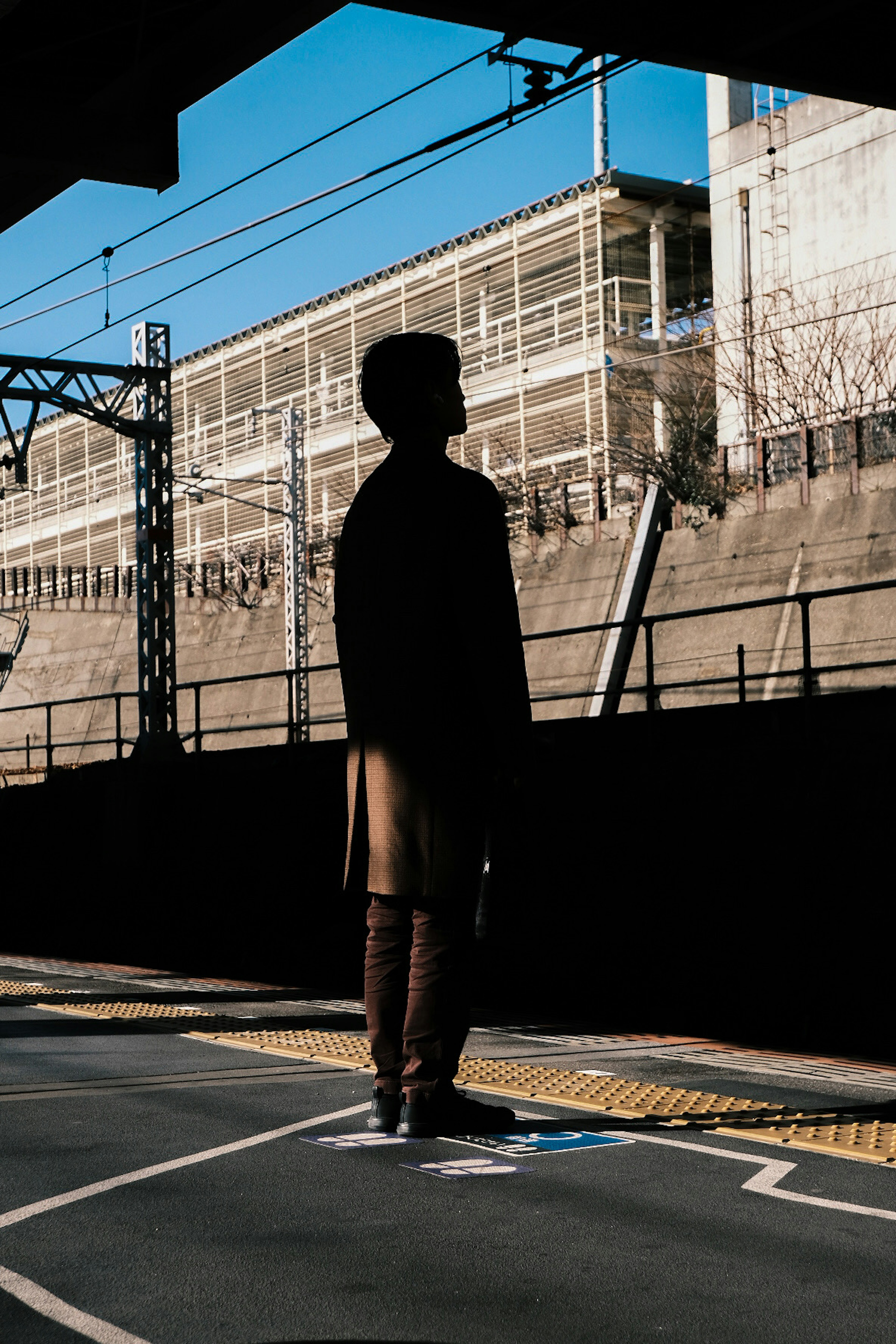 駅のプラットフォームに立つシルエットの人物と青空